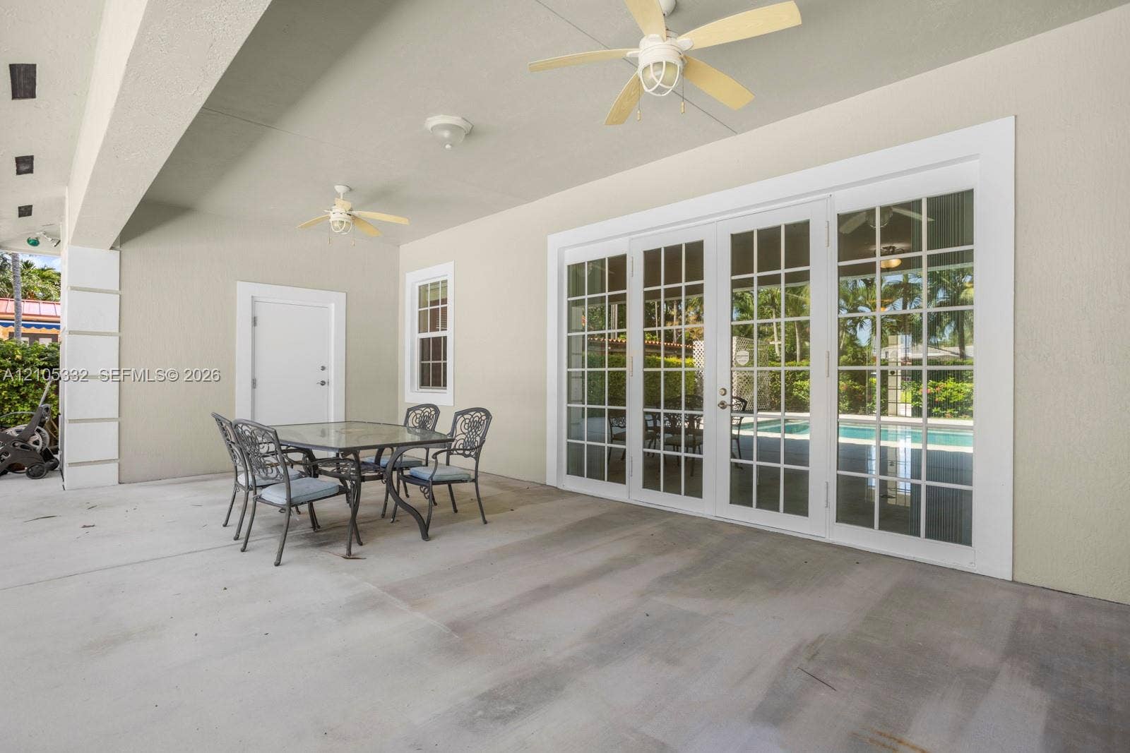 Spacious covered patio with concrete flooring, multiple ceiling fans, and large French doors