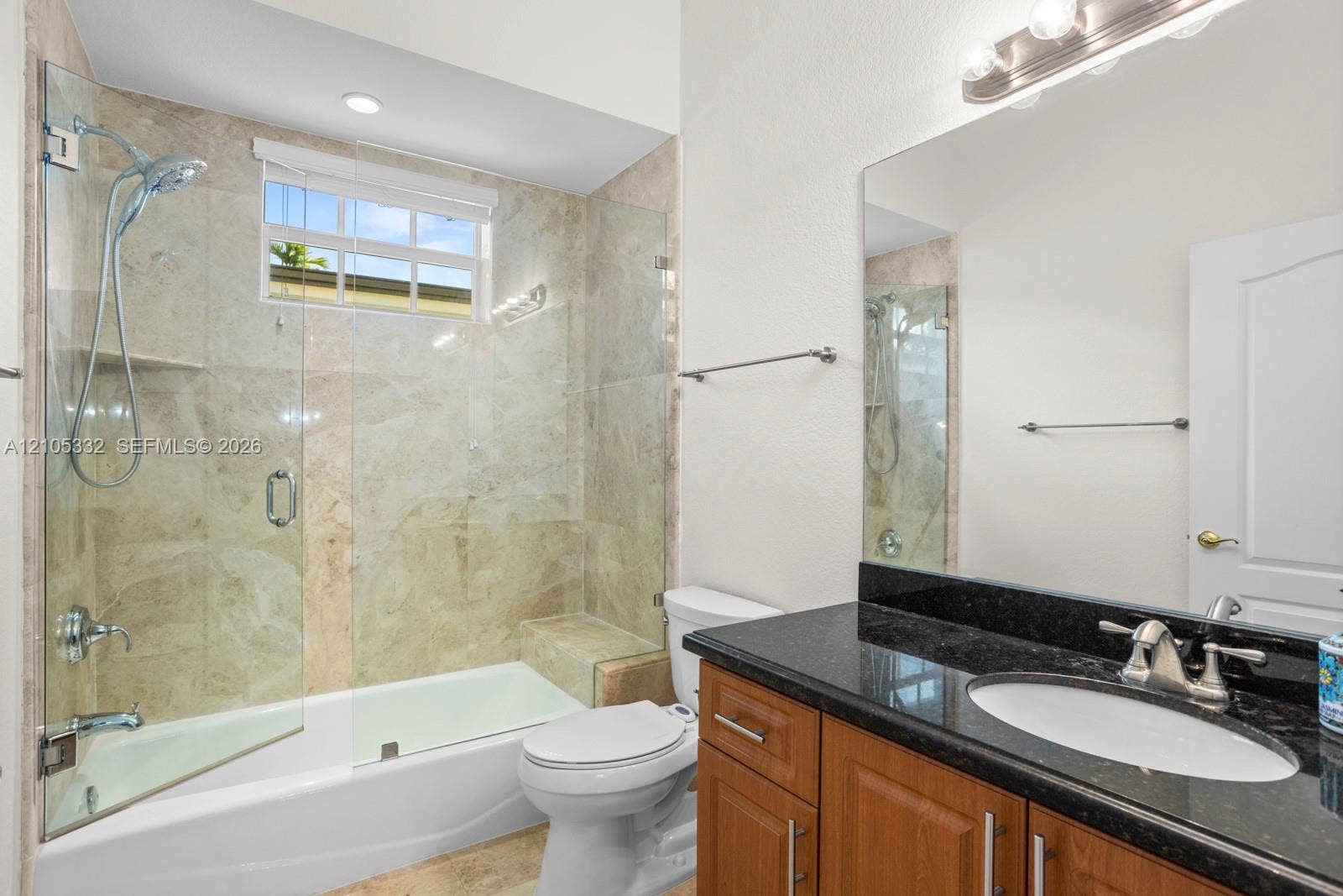 Tiled shower/tub combination with glass enclosure, wood-finish vanity with dark stone countertop, and integrated sink