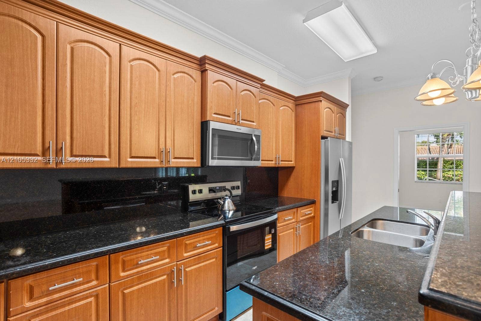 Kitchen featuring wood cabinetry, dark stone countertops, stainless steel appliances, and a double basin sink