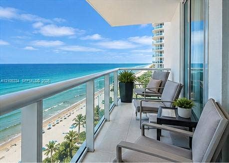 Balcony featuring a glass panel railing, tile flooring, and direct oceanfront scenery