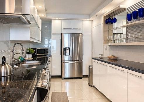 Modern kitchen with white cabinetry, stainless steel appliances, dark stone countertops, and tile flooring