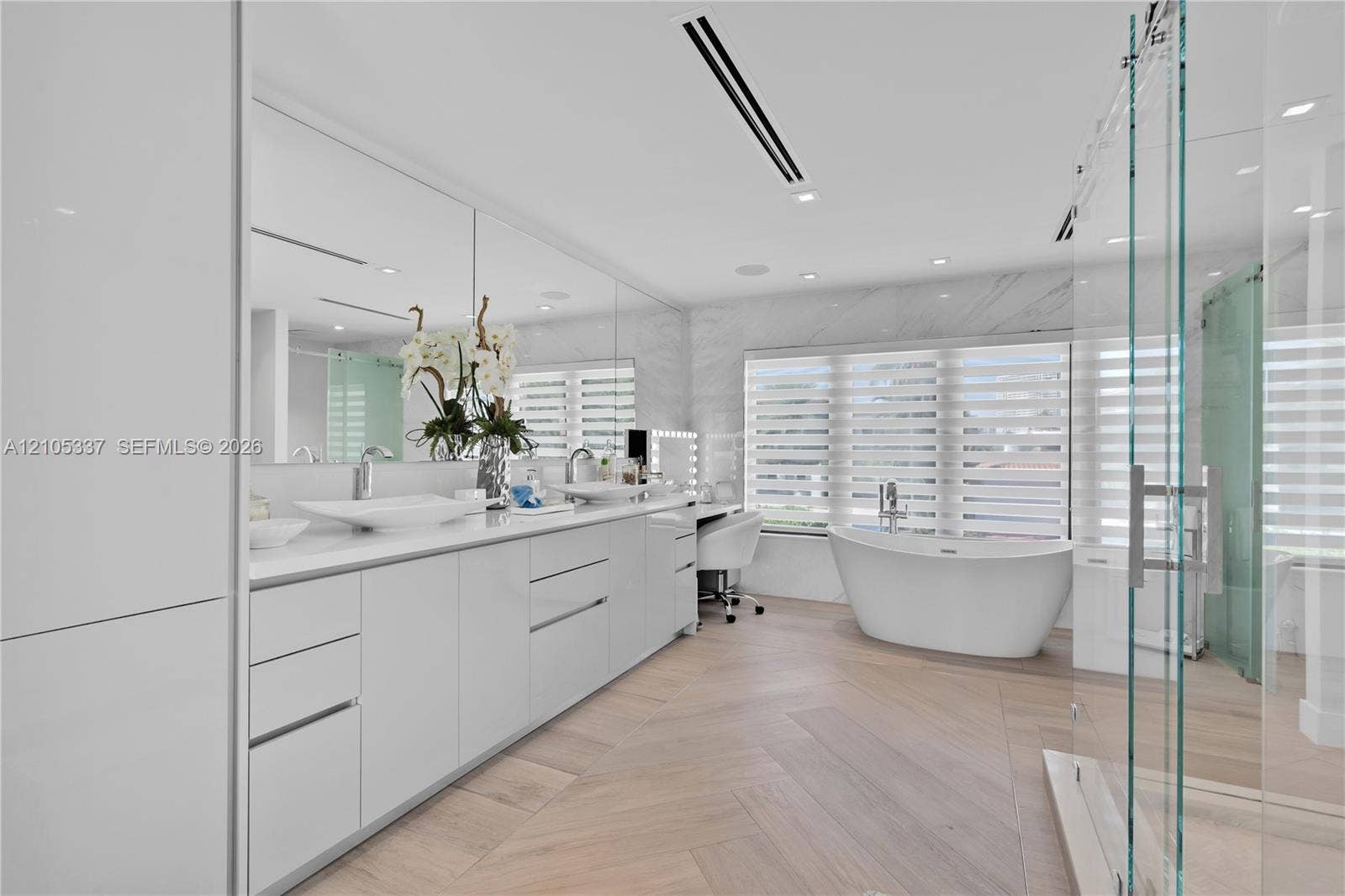 3322 NE 166th Street, North Miami Beach, FL 33160 Dual vanity featuring vessel sinks, stone-surface countertop, floor-to-ceiling mirror, freestanding soaking tub, and herringbone wood-finish flooring