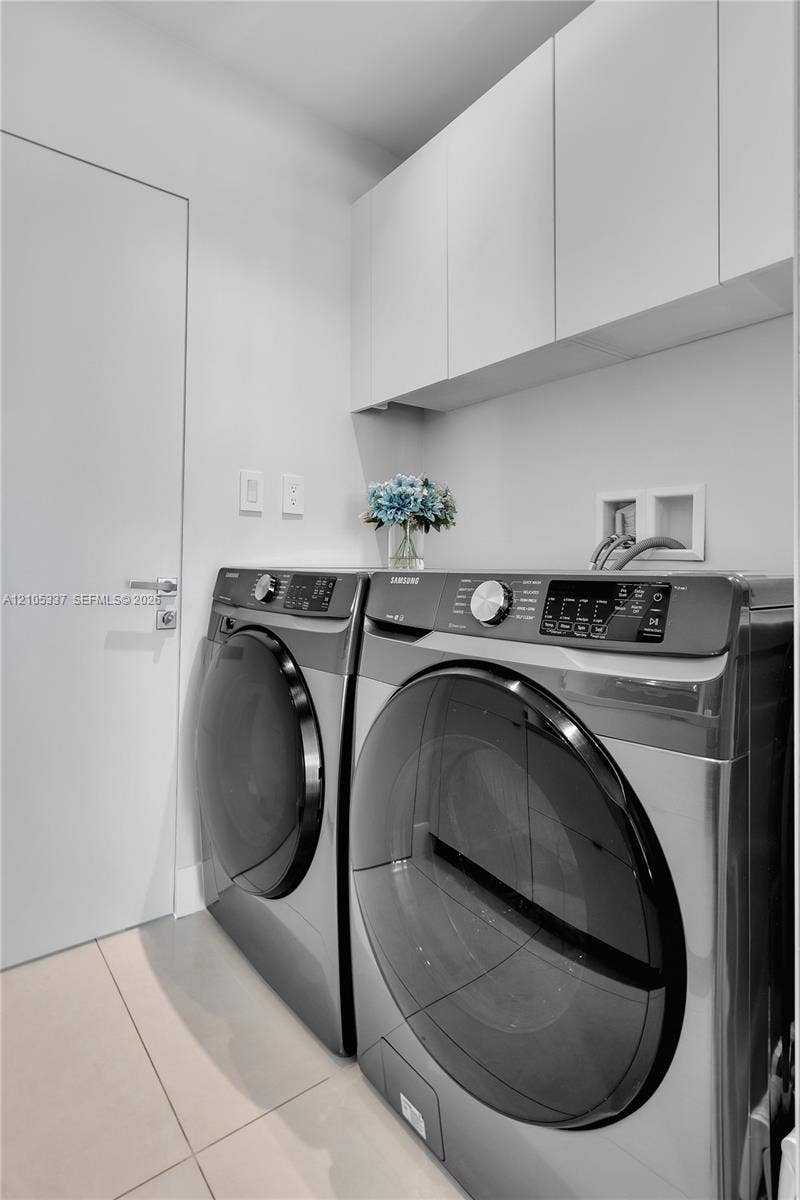 3322 NE 166th Street, North Miami Beach, FL 33160 Laundry area featuring flat-panel upper cabinetry, neutral large-format tile flooring, and a sleek solid-core door with modern brushed-metal hardware