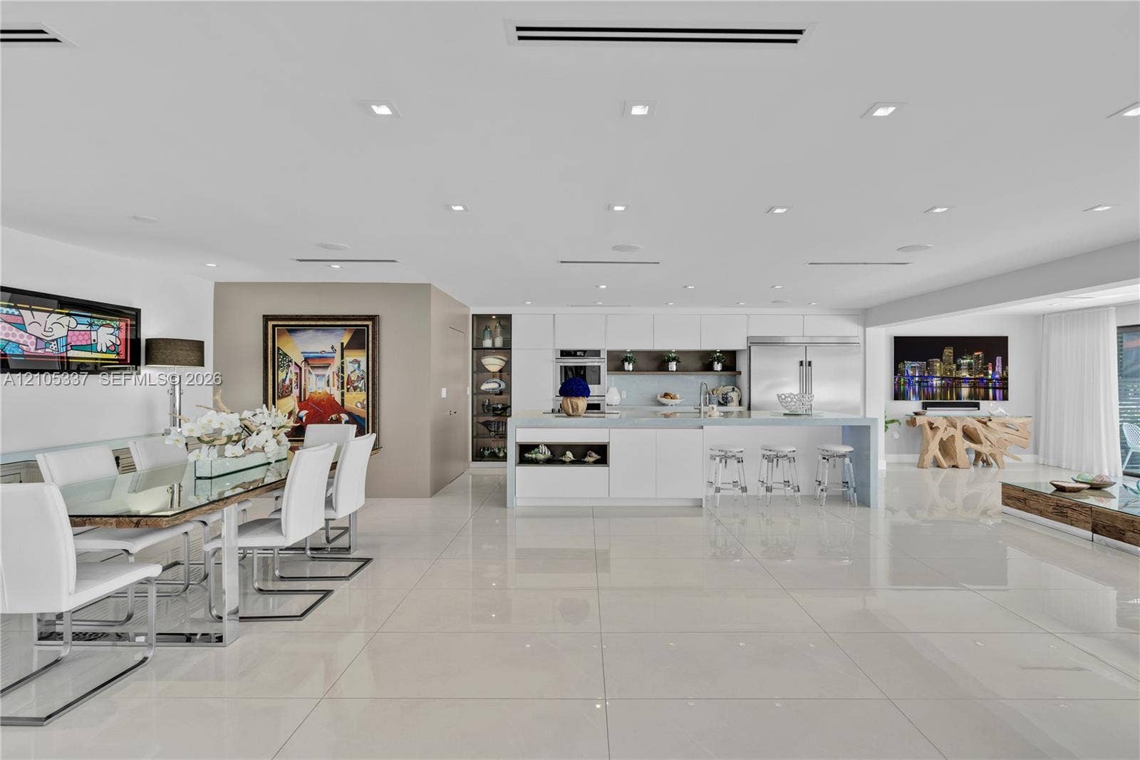 3322 NE 166th Street, North Miami Beach, FL 33160 Open-concept kitchen featuring minimalist white cabinetry, a large central island with seating, polished stone-finish flooring, and recessed ceiling lighting