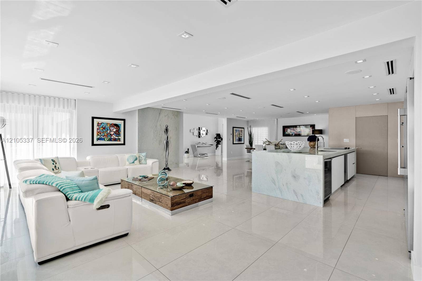 3322 NE 166th Street, North Miami Beach, FL 33160 Open-concept interior featuring large-format tile flooring, recessed ceiling lighting, a waterfall-edge kitchen island, and a full-height stone fireplace surround