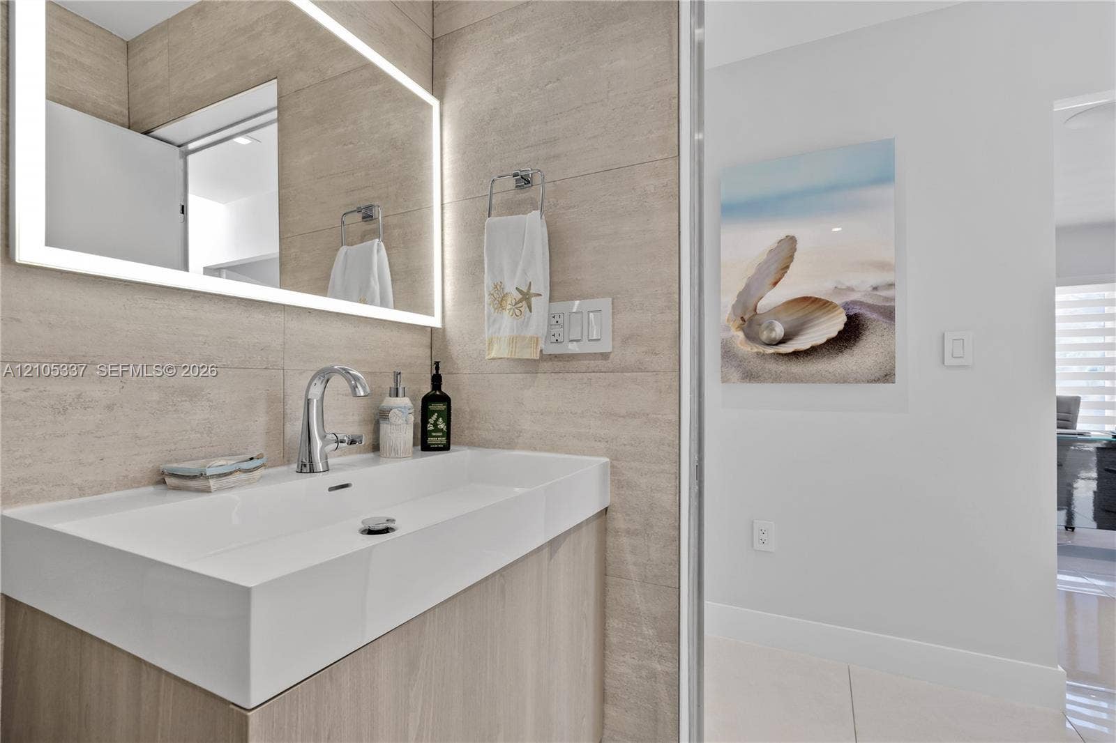 3322 NE 166th Street, North Miami Beach, FL 33160 Floating vanity featuring an integrated rectangular sink, wall-mounted polished chrome faucet, and backlit LED mirror, set against large-format neutral wall tile