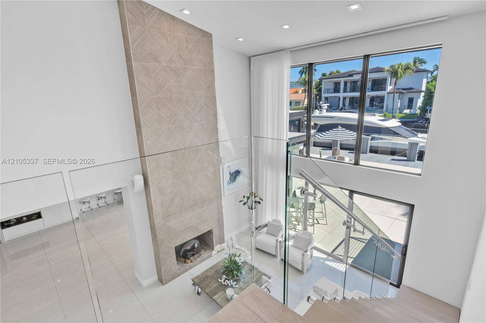 3322 NE 166th Street, North Miami Beach, FL 33160 Double-height living area featuring floor-to-ceiling windows, full-height decorative tile fireplace surround, recessed lighting, and glass panel stair railing