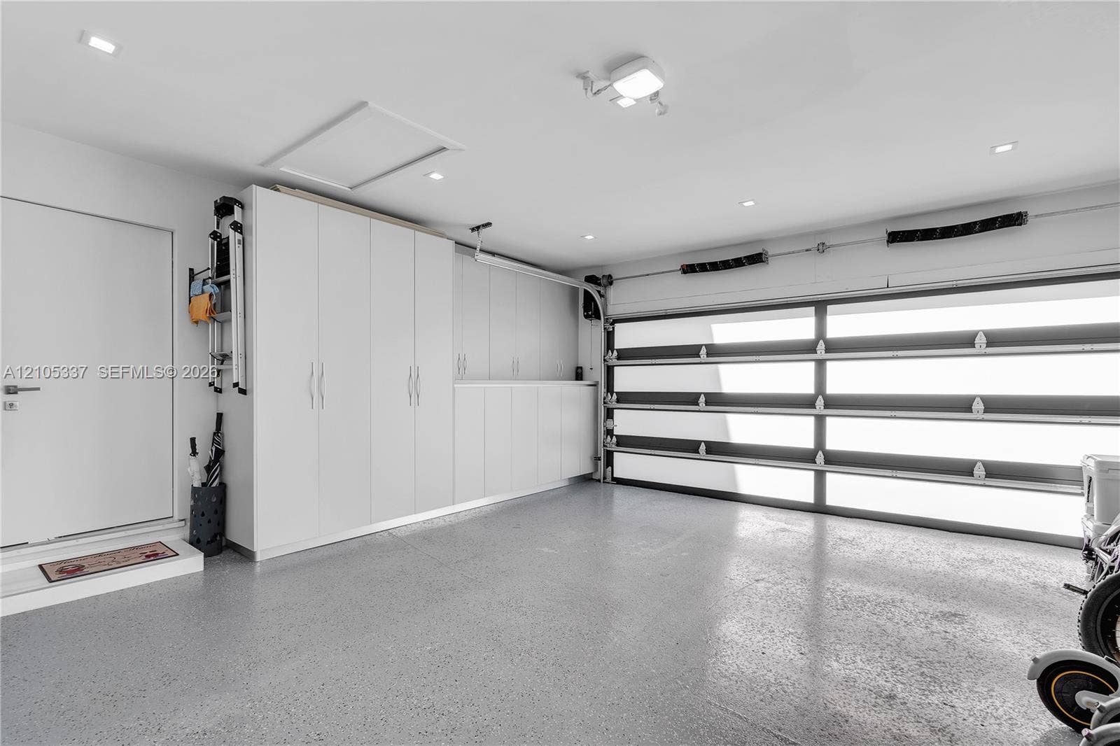 3322 NE 166th Street, North Miami Beach, FL 33160 Garage featuring a sectional door with frosted glass panels, built-in floor-to-ceiling cabinetry, recessed lighting, and speckled epoxy flooring