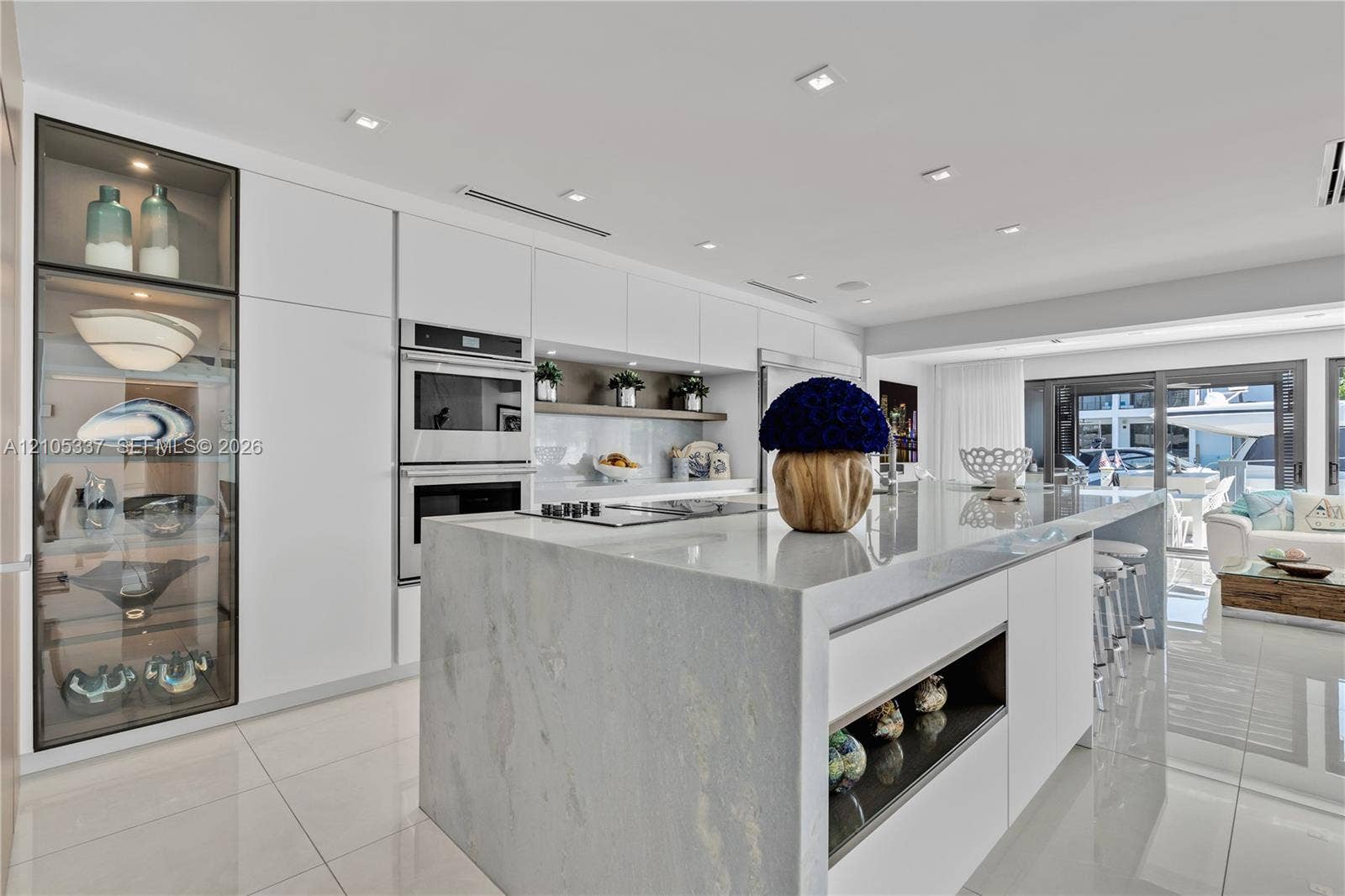 3322 NE 166th Street, North Miami Beach, FL 33160 Modern kitchen featuring floor-to-ceiling glass-front cabinetry, a waterfall-edge stone island, built-in dual wall ovens, recessed ceiling lighting, and tile flooring