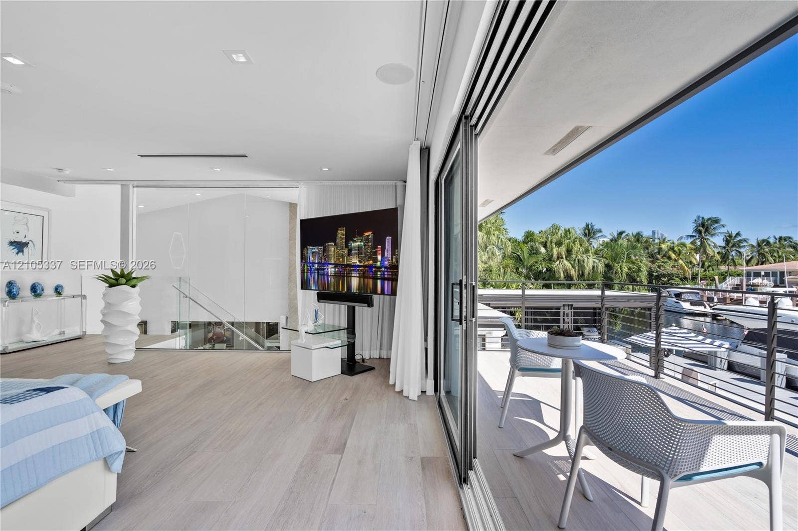 3322 NE 166th Street, North Miami Beach, FL 33160 Floor-to-ceiling retractable glass doors, expansive covered balcony with cable railing, wood-finish flooring, and recessed ceiling lighting
