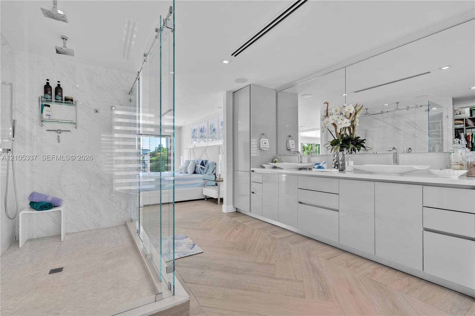 3322 NE 166th Street, North Miami Beach, FL 33160 Herringbone wood-finish flooring, glass-enclosed walk-in shower with dual rainfall showerheads, high-gloss dual vanity cabinetry, and large-format wall-mounted mirror
