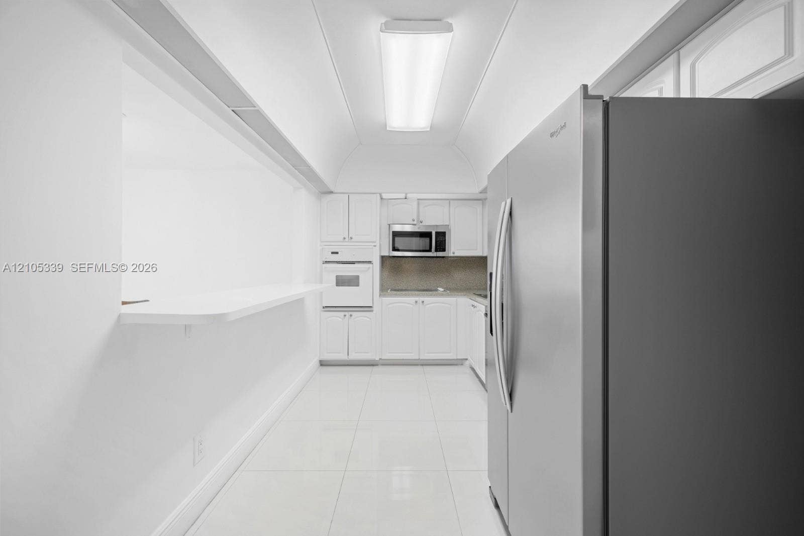 White cabinetry, white countertops, built-in microwave, built-in oven, and stainless steel refrigerator