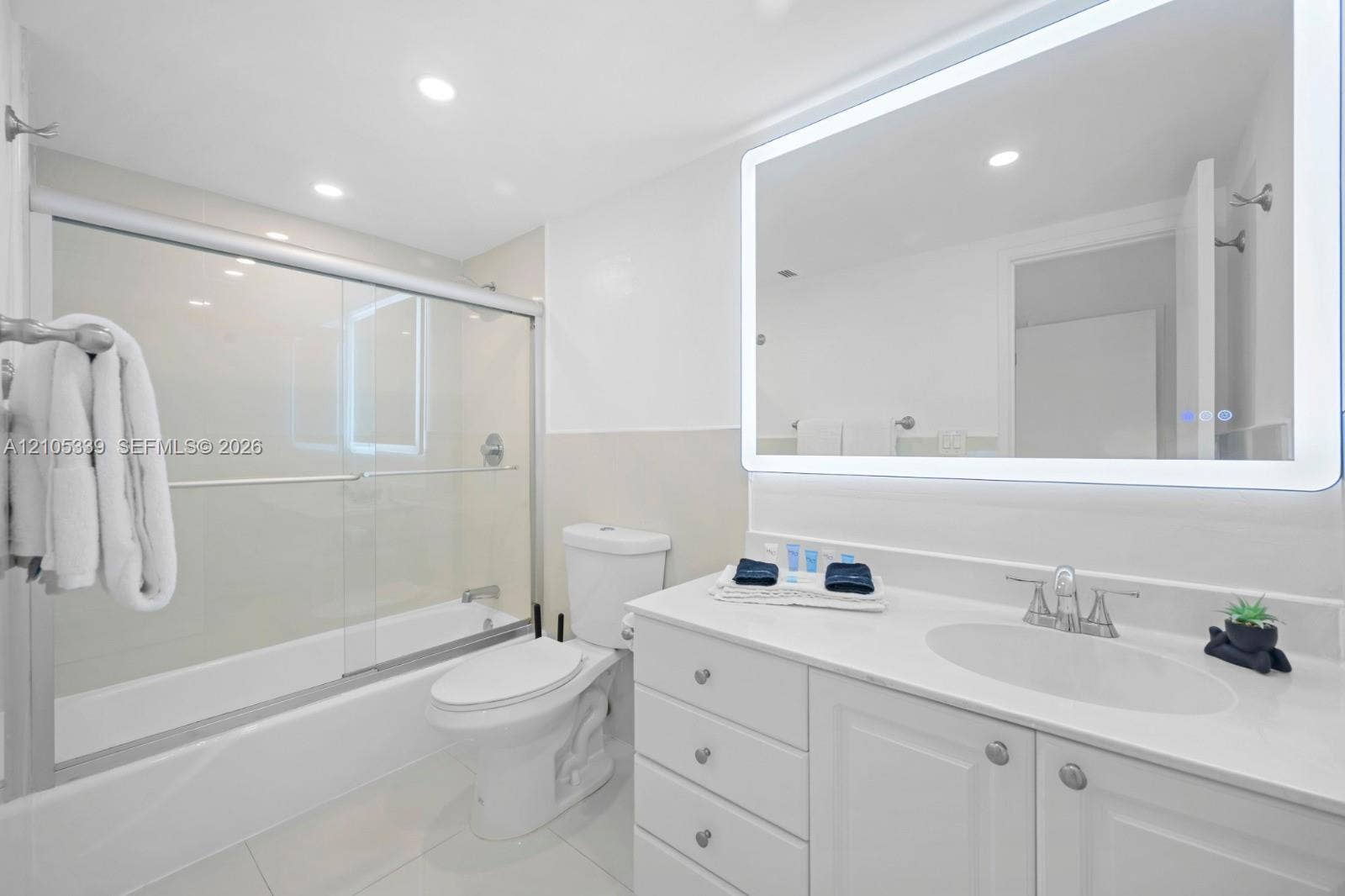 Bathroom featuring a white vanity with cabinet storage, integrated sink, and a large illuminated mirror