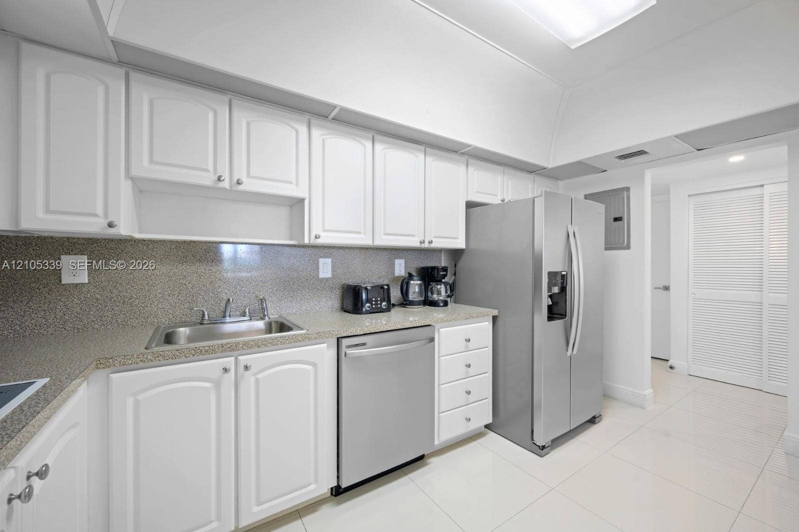 White cabinetry with silver hardware, speckled countertops, stainless steel appliances, and tile flooring