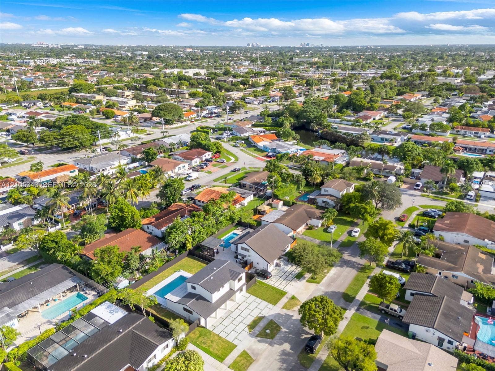 Aerial perspective of a multi-story residence featuring a private swimming pool, concrete paver driveway, and mature landscaping