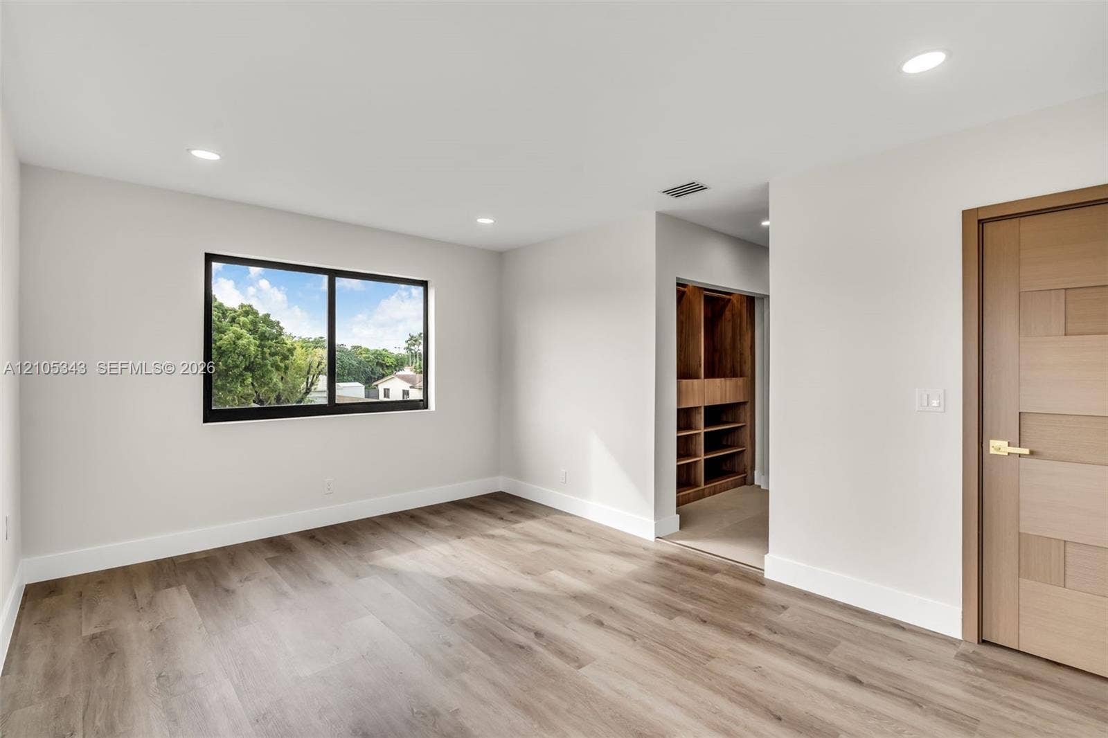Room featuring wood-finish flooring, recessed lighting, a horizontal sliding window with a dark frame, and a wood-finished door with metallic hardware, complemented by a built-in wooden closet system