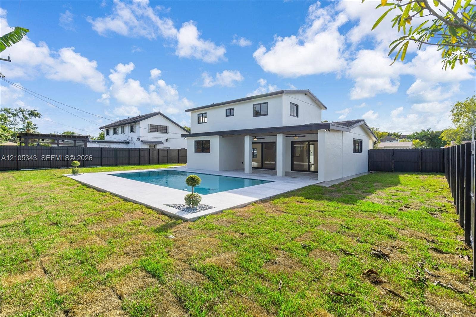 Two-story residence featuring a covered patio, swimming pool with light-toned hardscaping, and full-height perimeter privacy fencing