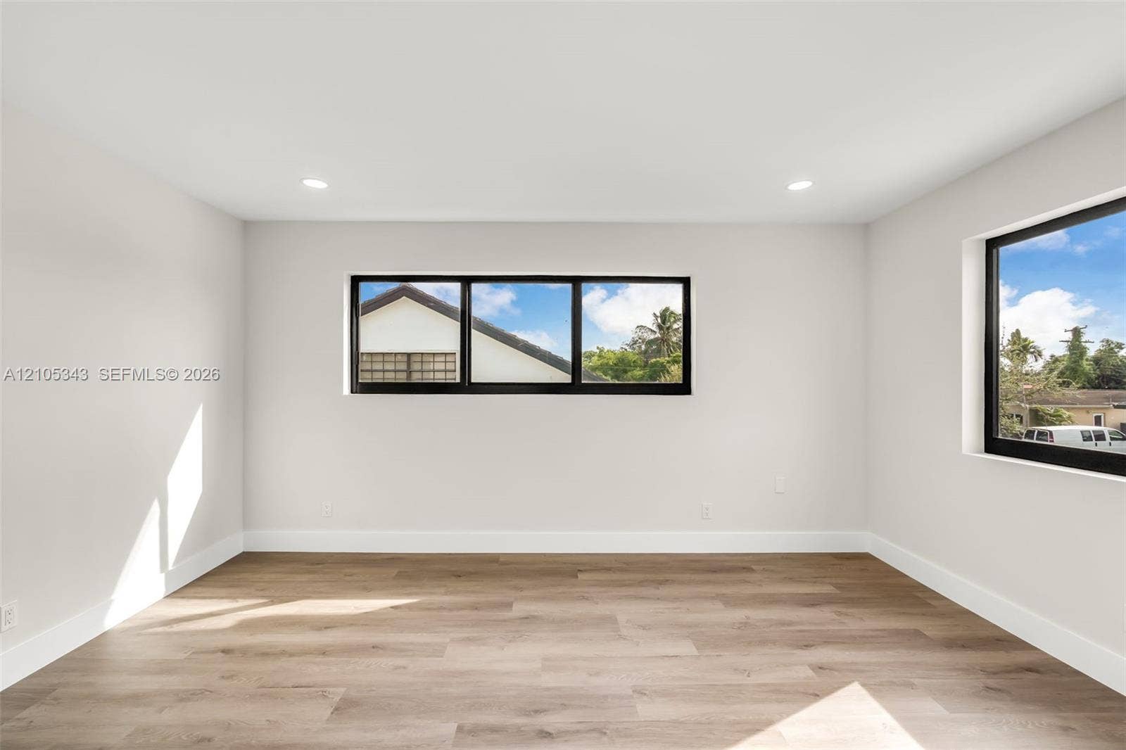 Neutral-toned interior space featuring wood-finish flooring, recessed lighting, and windows with black frames