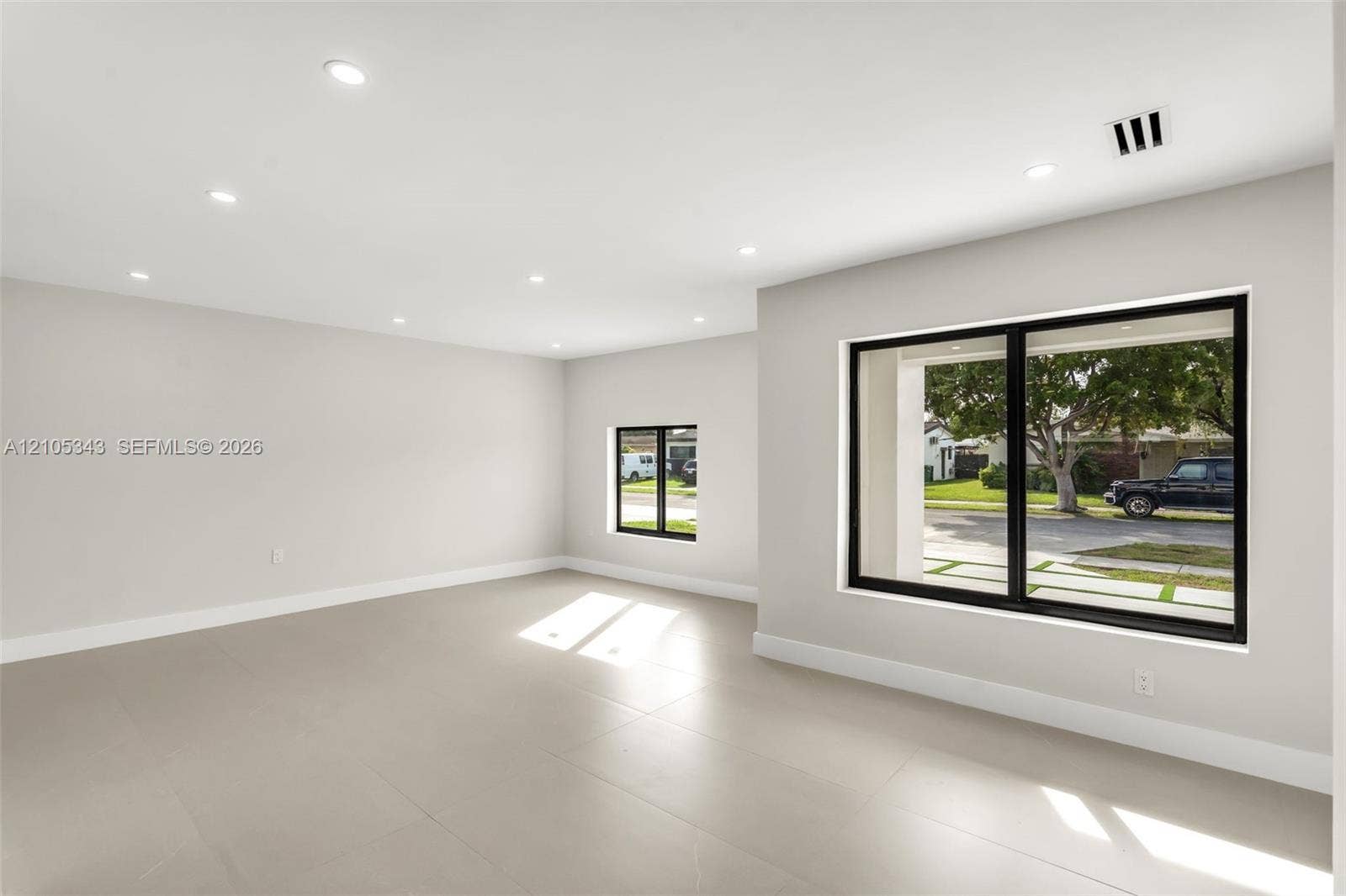 Neutral-toned interior space featuring oversized rectangular tile flooring, recessed ceiling lighting, and black-framed windows
