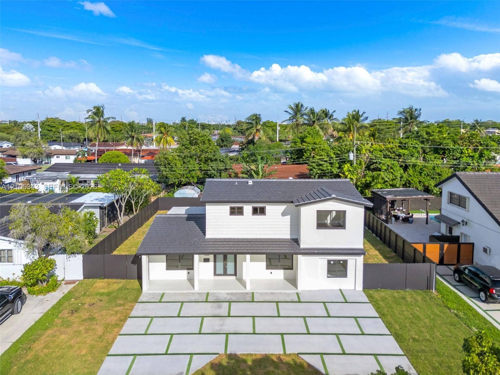 Two-story exterior featuring white horizontal siding, a dark-toned roof, a covered front porch, and a paved grid-pattern driveway with integrated turf strips, all enclosed by dark perimeter fencing