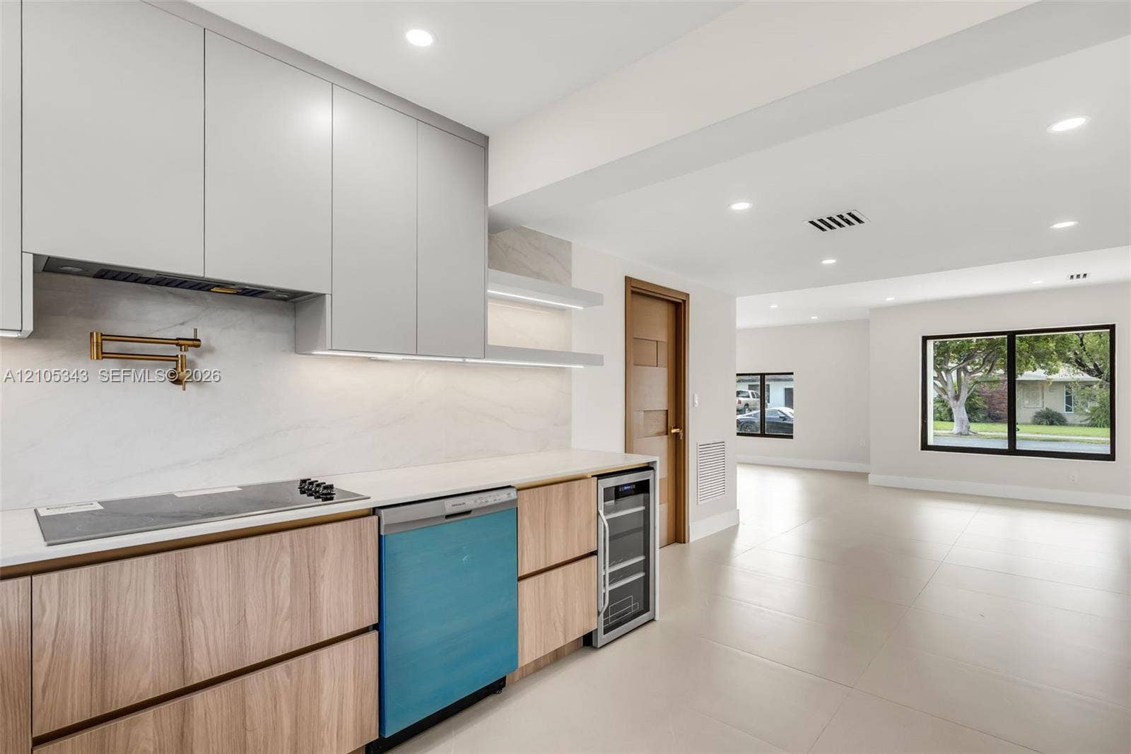 Kitchen featuring custom flat-panel cabinetry, light-toned stone-finish backsplash, built-in beverage refrigerator, wall-mounted pot filler, and recessed lighting