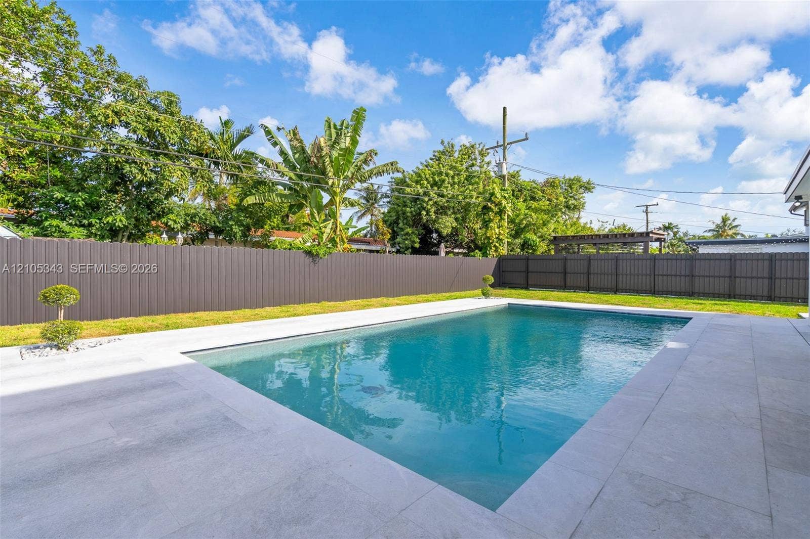 Rectangular swimming pool featuring a light-toned stone deck, surrounding privacy fencing, and a manicured lawn