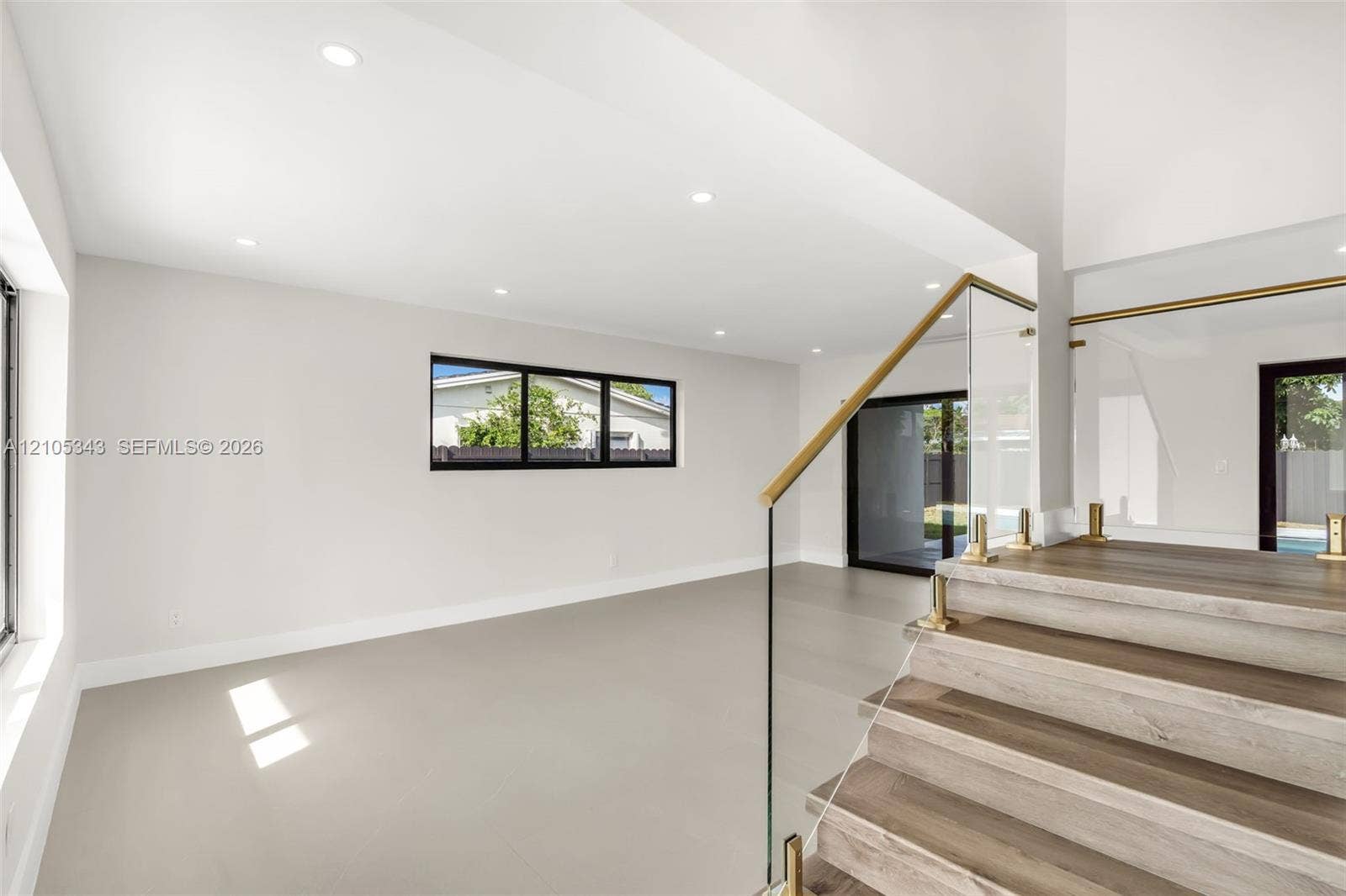 Open-concept interior featuring wood-finish tread staircase with glass panel railing and brass-finish hardware, recessed lighting, and large-format tile flooring