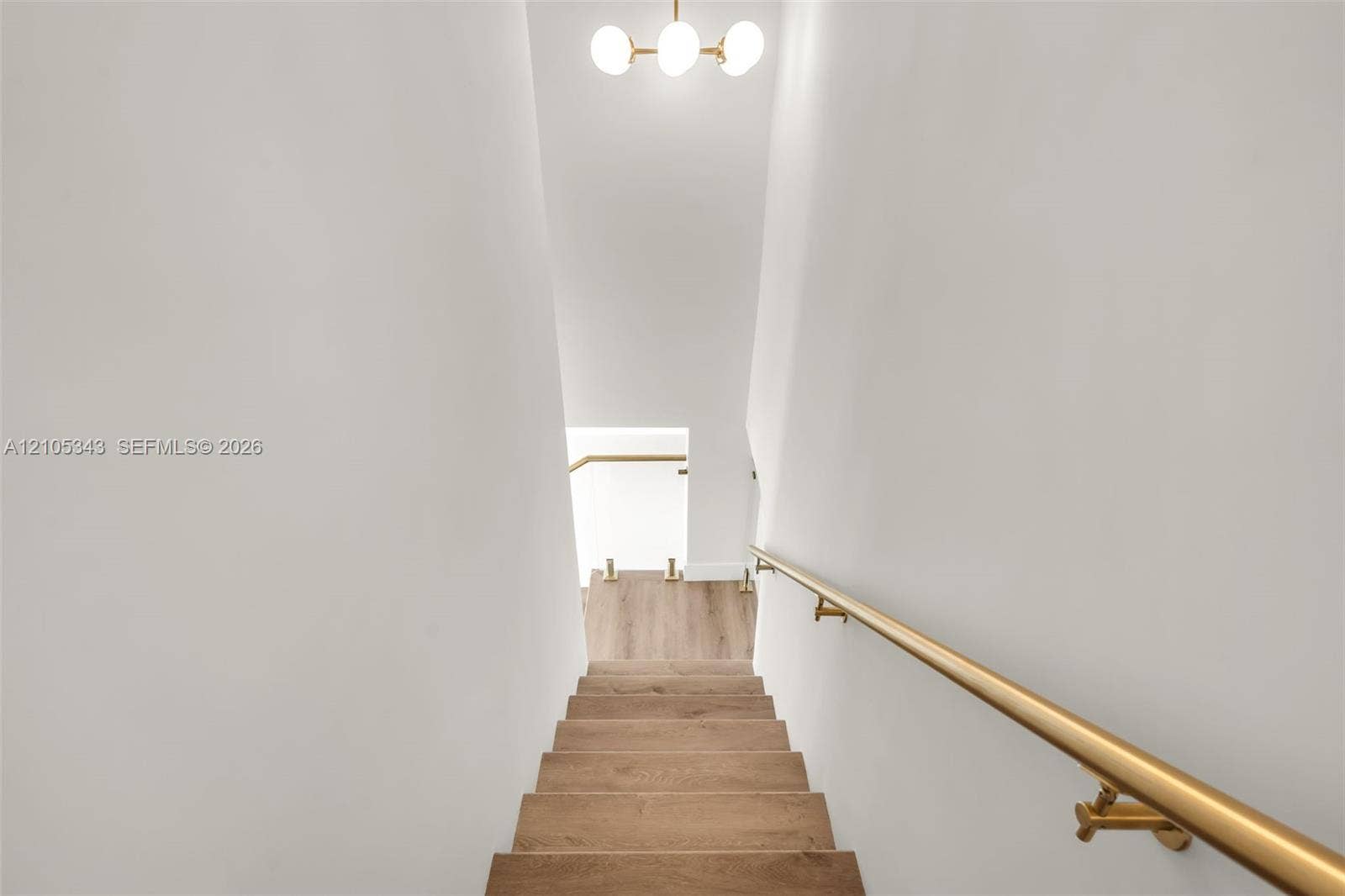 Staircase featuring wood-finish treads, a metallic gold-tone handrail, glass balustrade panel, and a three-globe pendant light fixture