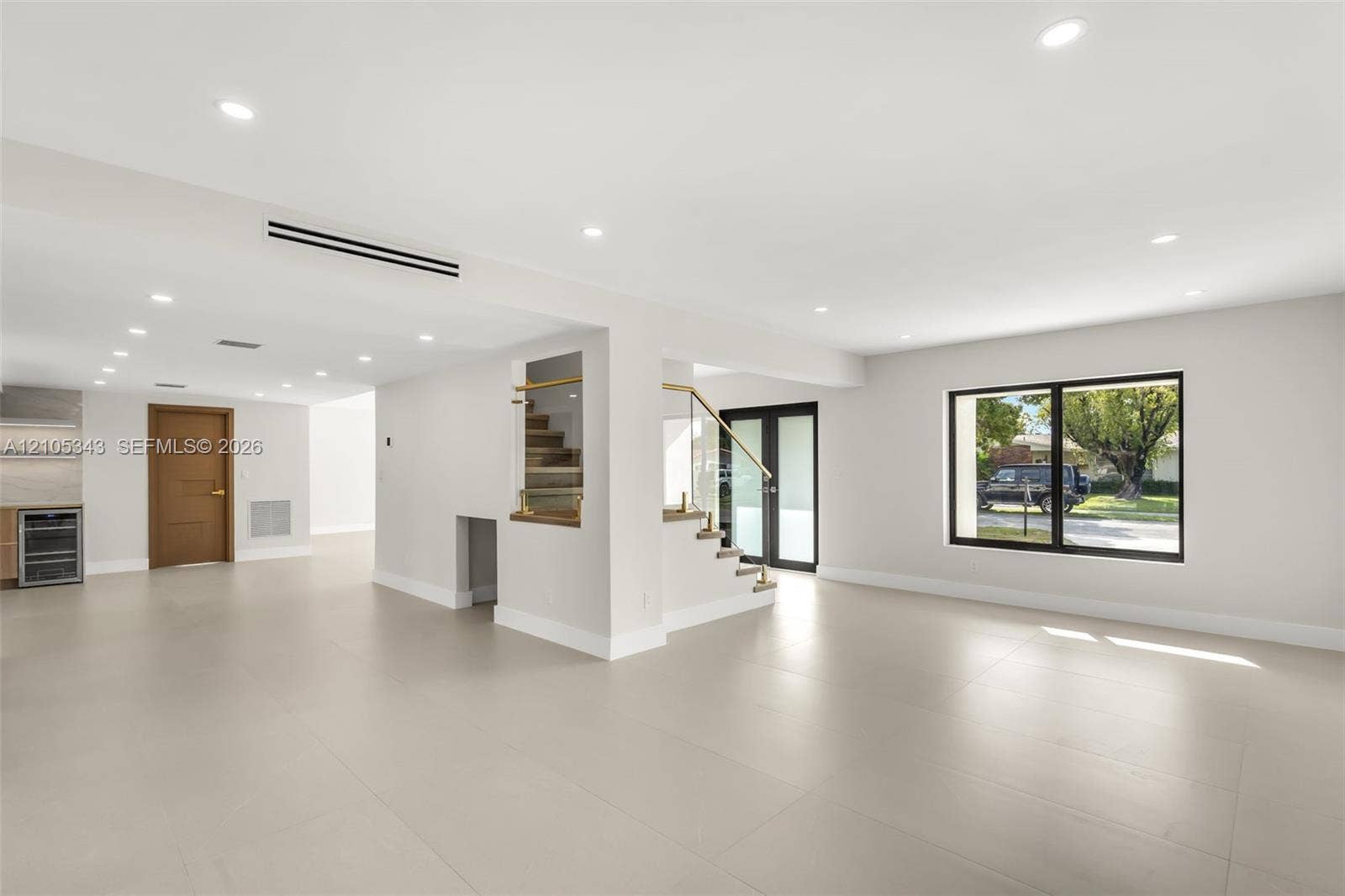 Large-format tile flooring, recessed ceiling lighting, staircase with glass railing, and black-framed exterior doors