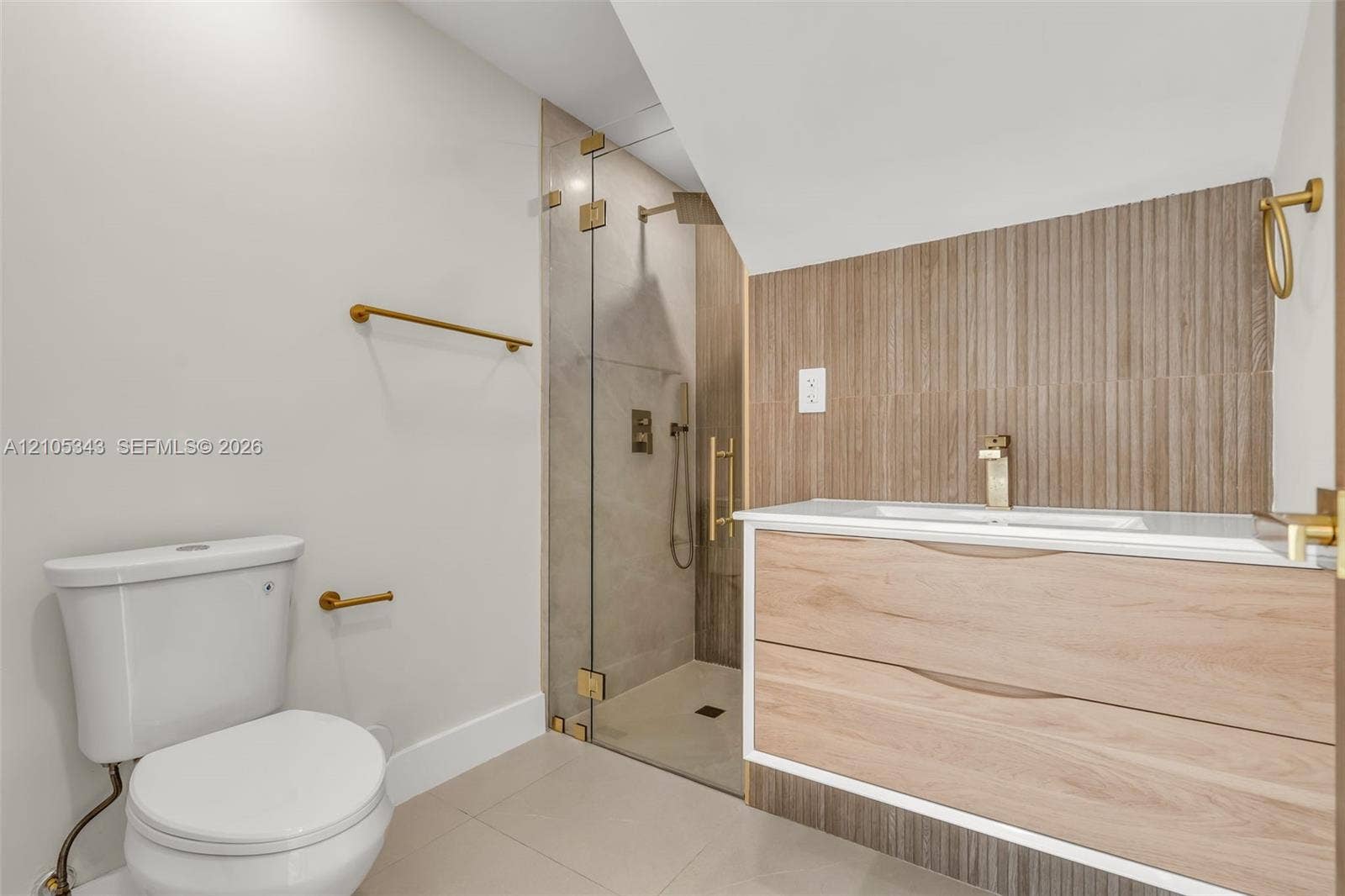 Floating wood-finish vanity with integrated sink, brass-tone hardware, vertical ribbed tile backsplash, and walk-in shower with glass enclosure