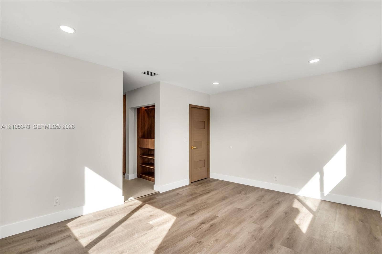 Neutral-toned walls, wood-finish flooring, recessed lighting, and a walk-in closet with built-in shelving