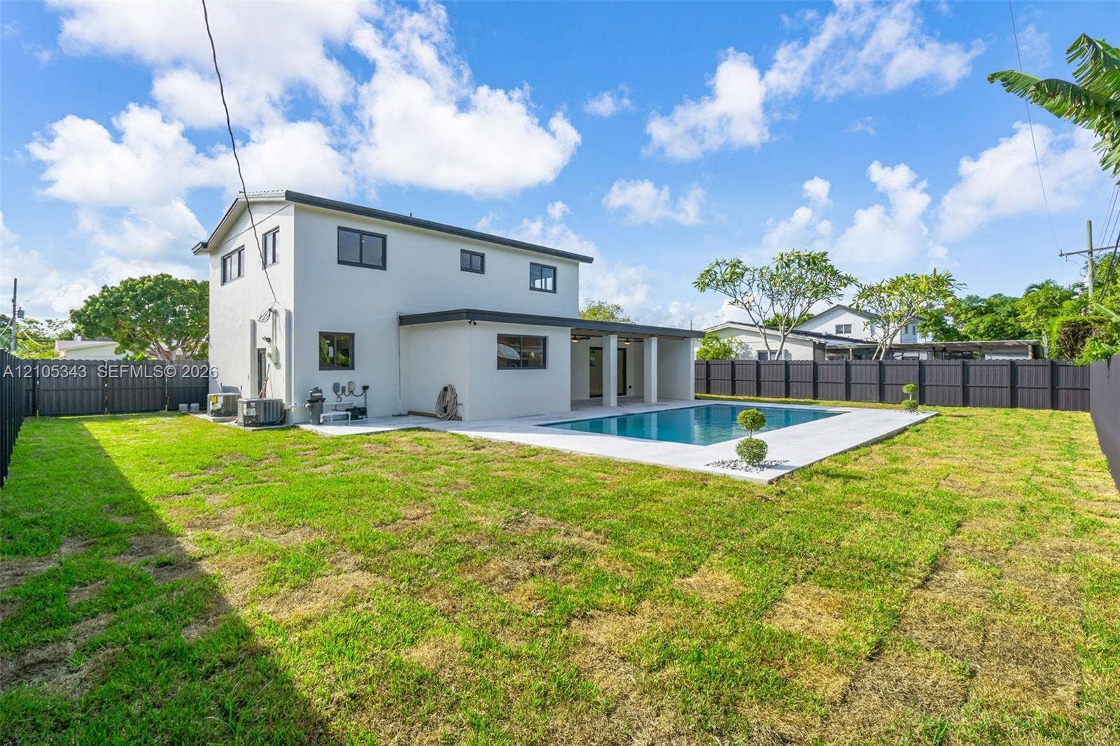 Rear exterior featuring a two-story light-toned facade, an in-ground swimming pool, a concrete pool deck, and perimeter privacy fencing