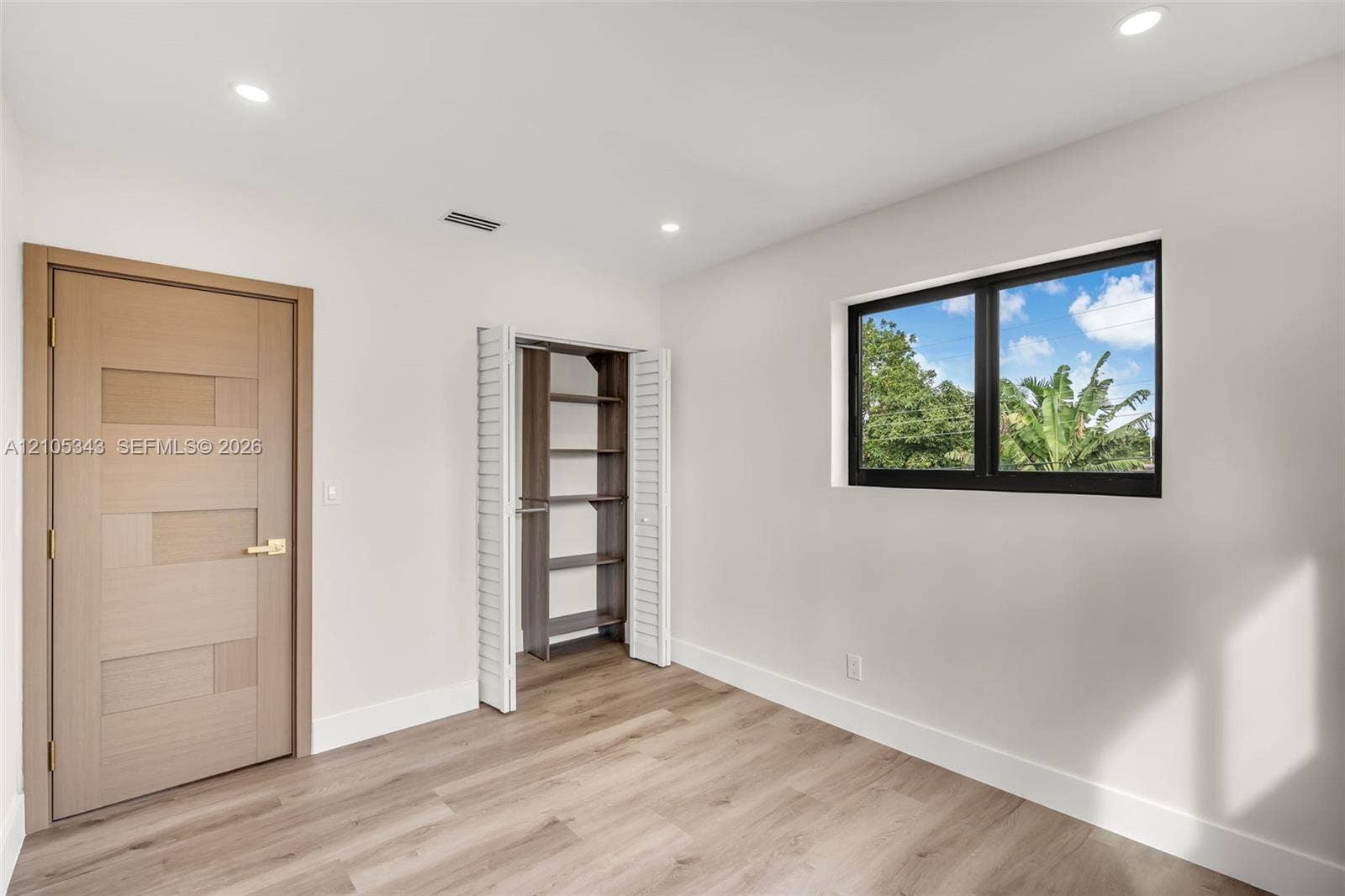 Wood-finish flooring, recessed lighting, interior door with a geometric paneled design, closet with built-in shelving, and a black-framed window