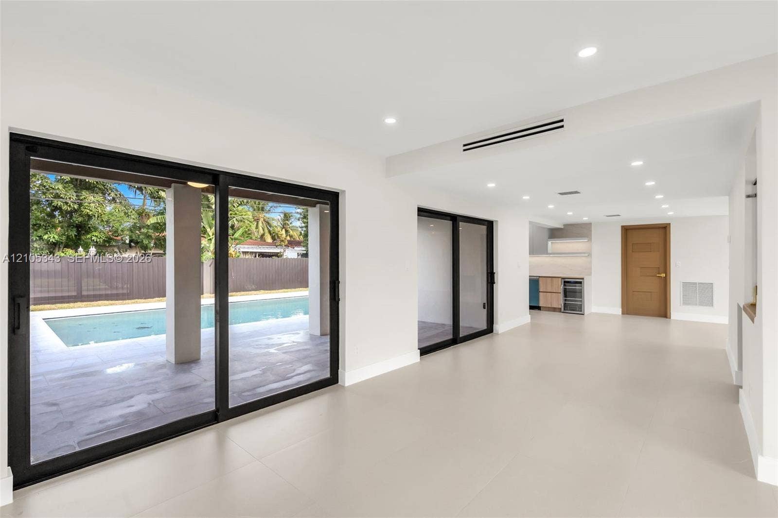 Large-format sliding glass doors with black frames, recessed ceiling lighting, light-toned tile flooring, and integrated kitchenette cabinetry