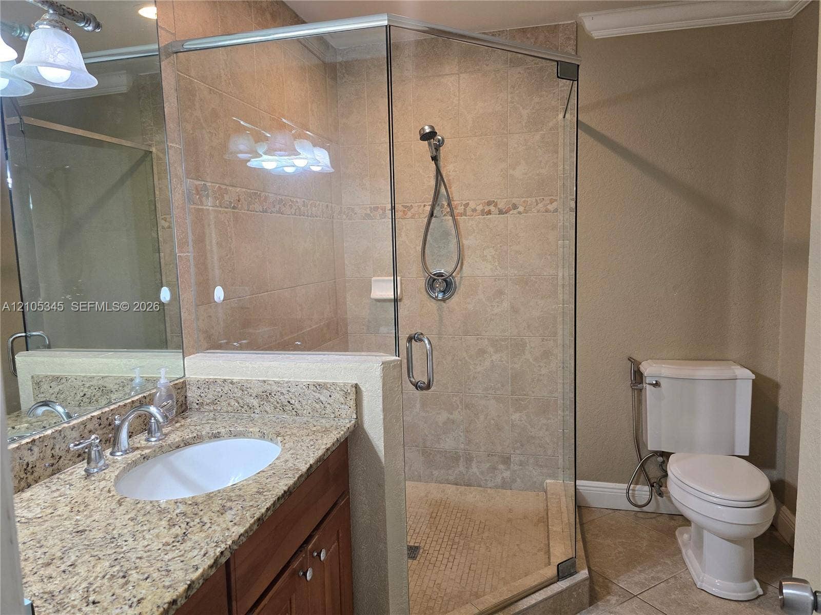 Vanity with stone countertop and undermount sink, glass-enclosed shower featuring tiled surround and handheld fixture, and neutral tile flooring