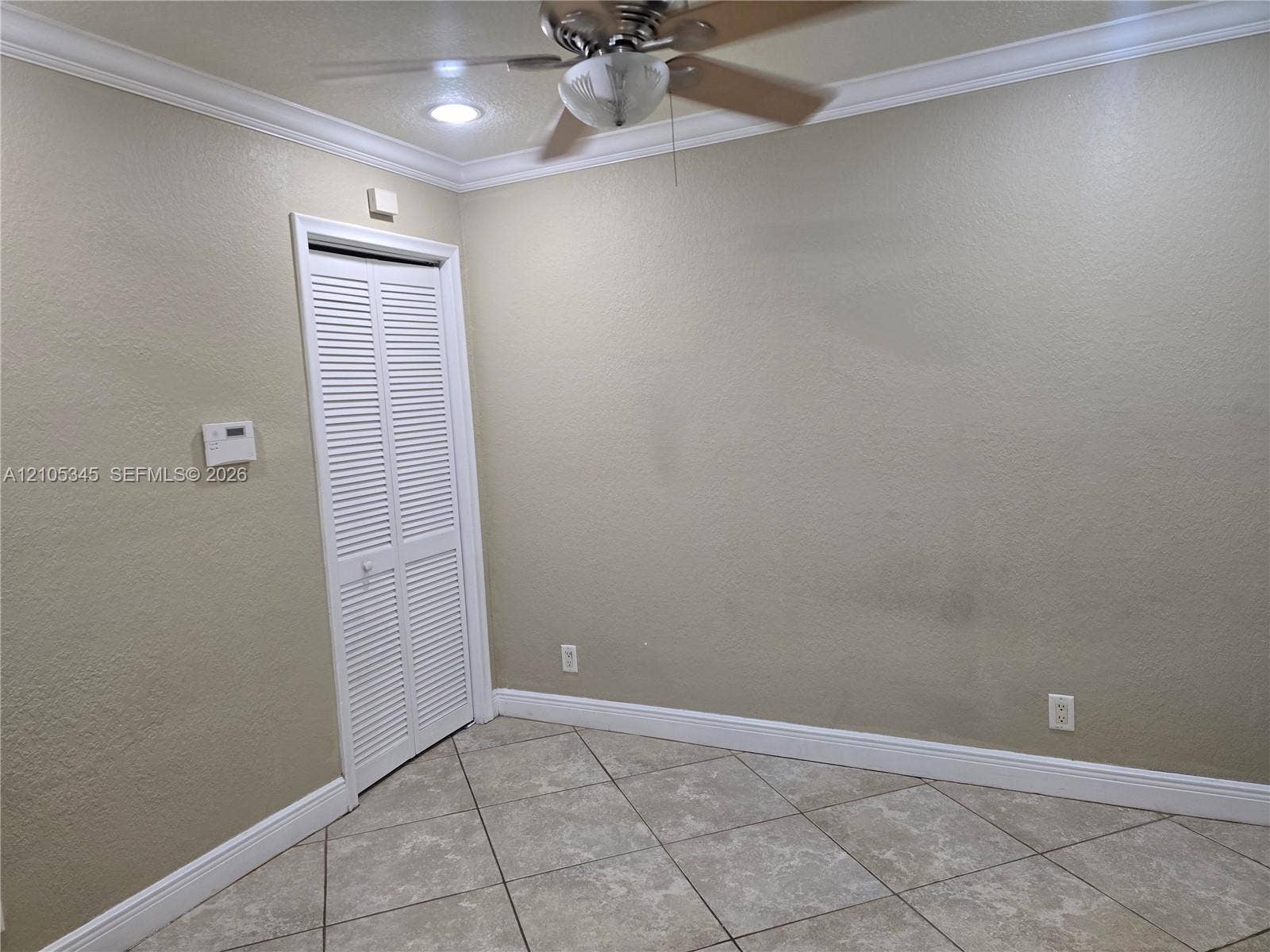 Room featuring neutral wall paint, tile flooring, crown molding, a ceiling fan with light fixture, and a louvered-style closet door