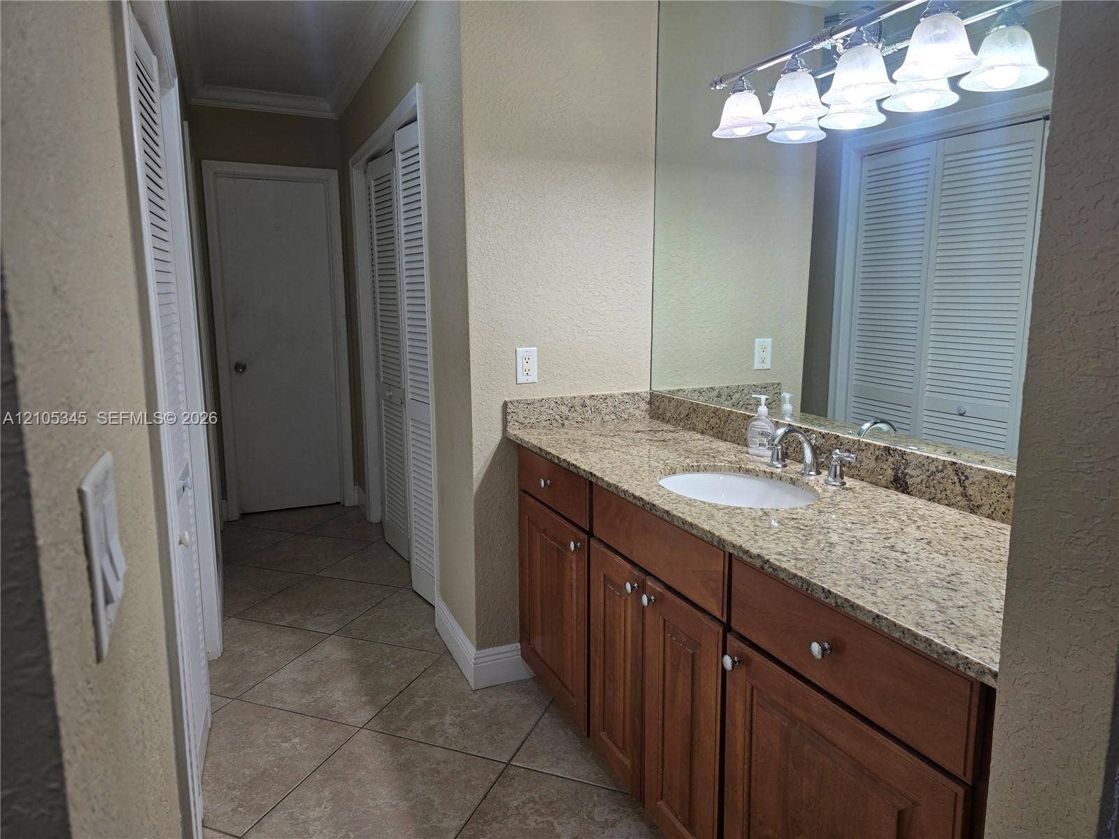 Vanity featuring stone-finish countertop with integrated sink, wood-finish cabinetry, full-width wall mirror, five-light fixture, and tile flooring