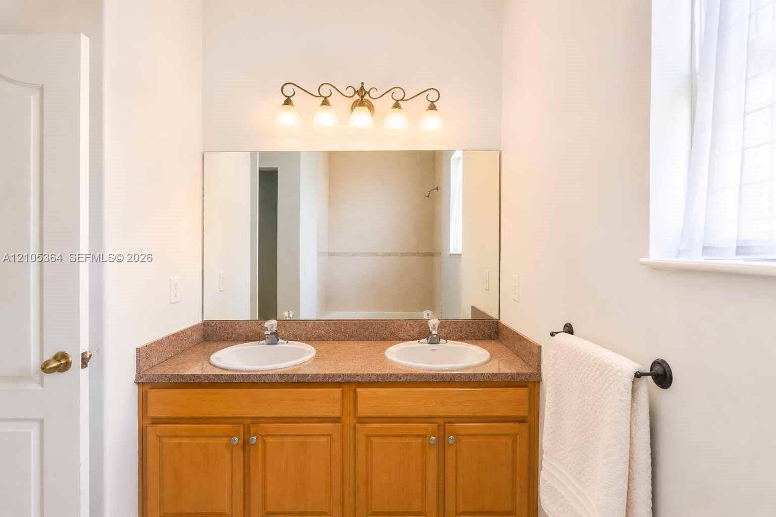 Dual vanity with integrated sinks, wood-finish cabinetry, and a large wall-mounted mirror