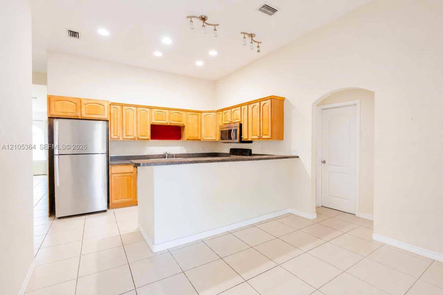 Kitchen featuring wood cabinetry, stainless steel appliances, dark countertops, and tile flooring