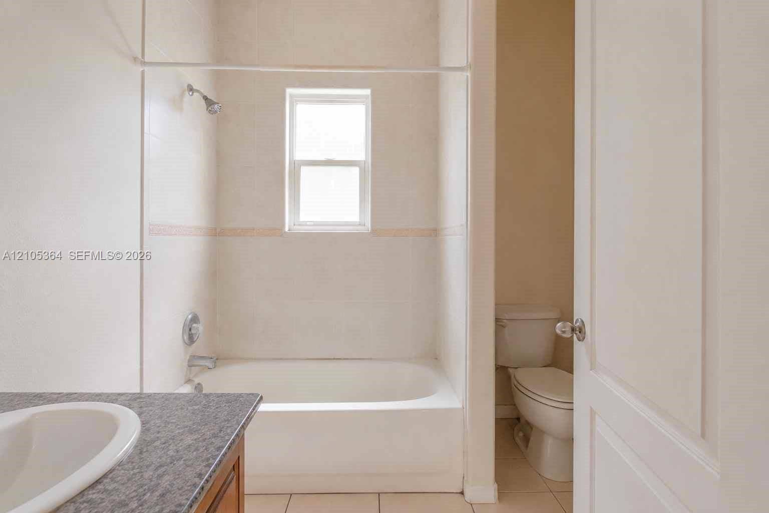 Bathtub with shower fixture, tiled surround with decorative accent, and a window