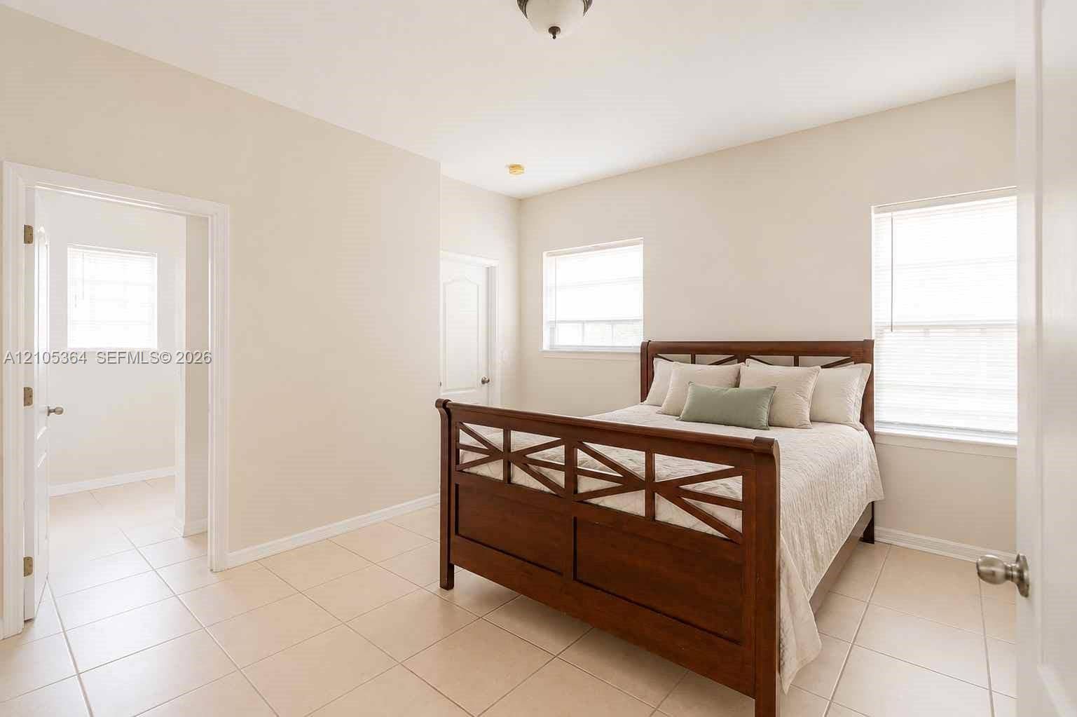 Light-toned tile flooring, two windows with blinds, a ceiling-mounted light fixture, and neutral wall tones