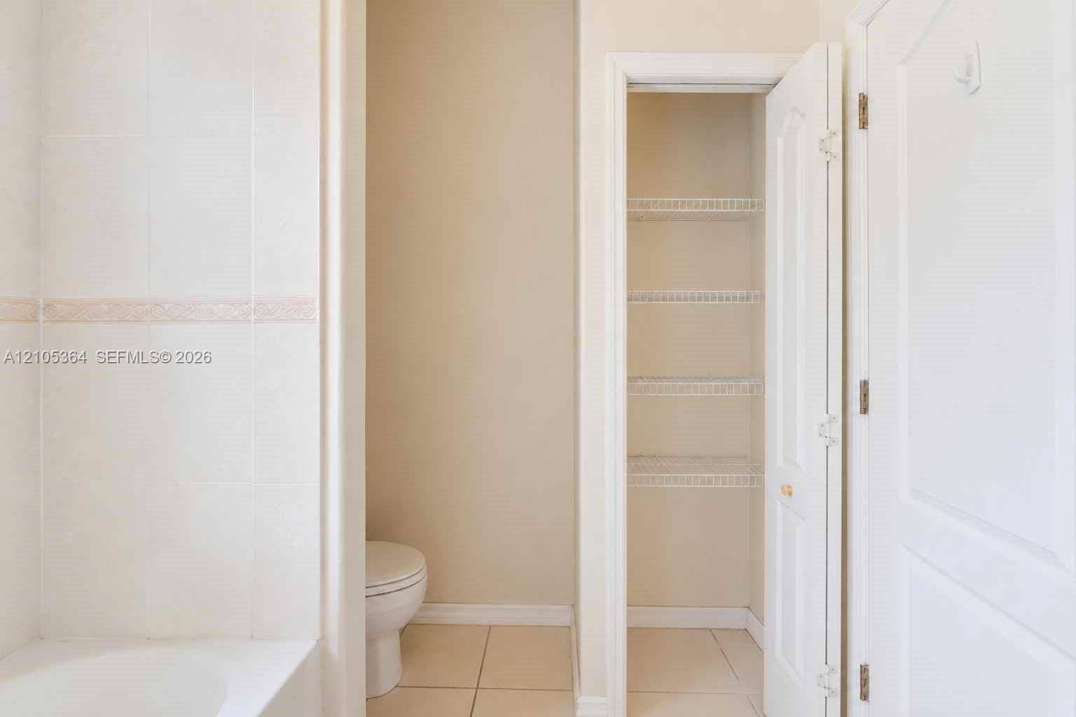 Built-in storage closet with wire shelving, white paneled door, and tile flooring