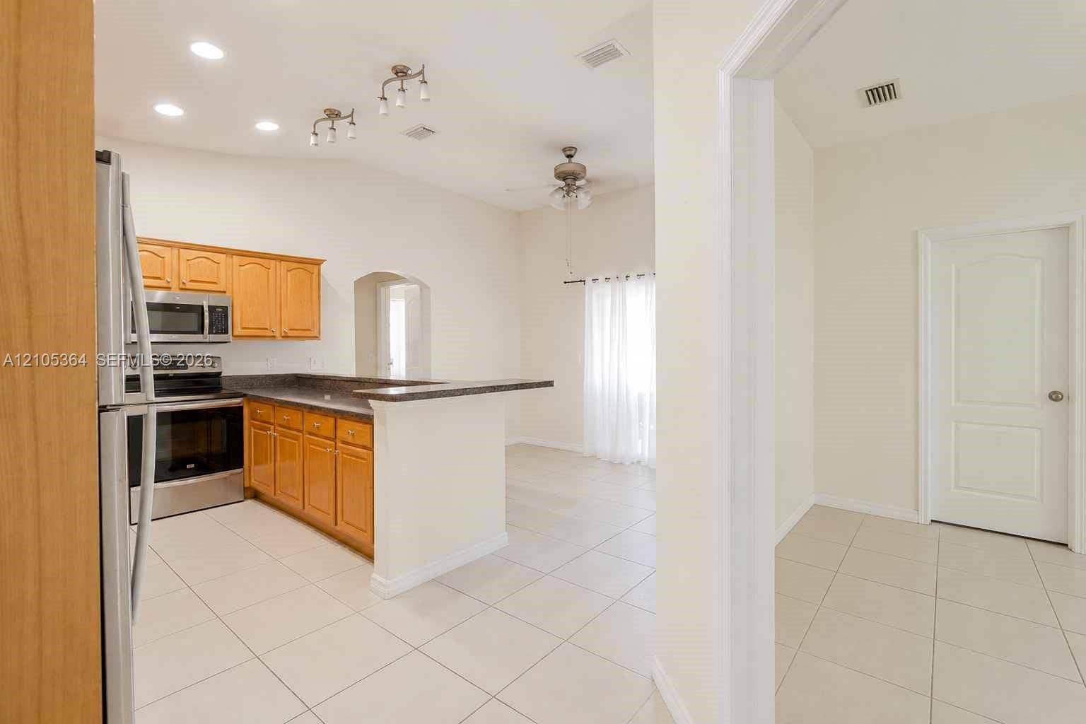 Kitchen featuring wood cabinetry, stainless steel appliances, dark countertops, and tile flooring