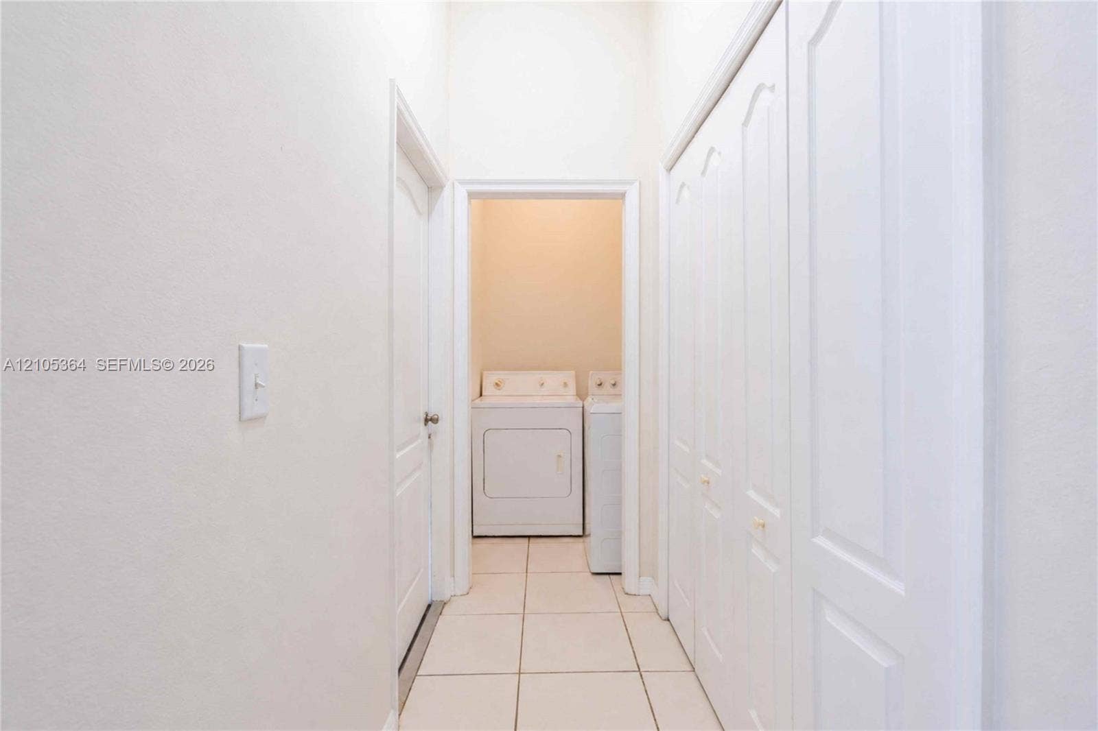 Hallway with light-colored tile flooring, white walls, and bi-fold closet doors