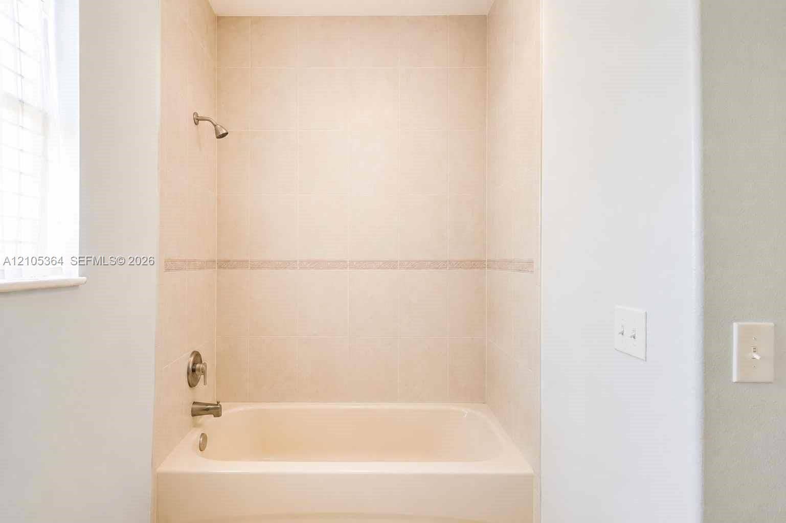 Built-in bathtub with a tile surround, decorative tile band, and polished chrome fixtures
