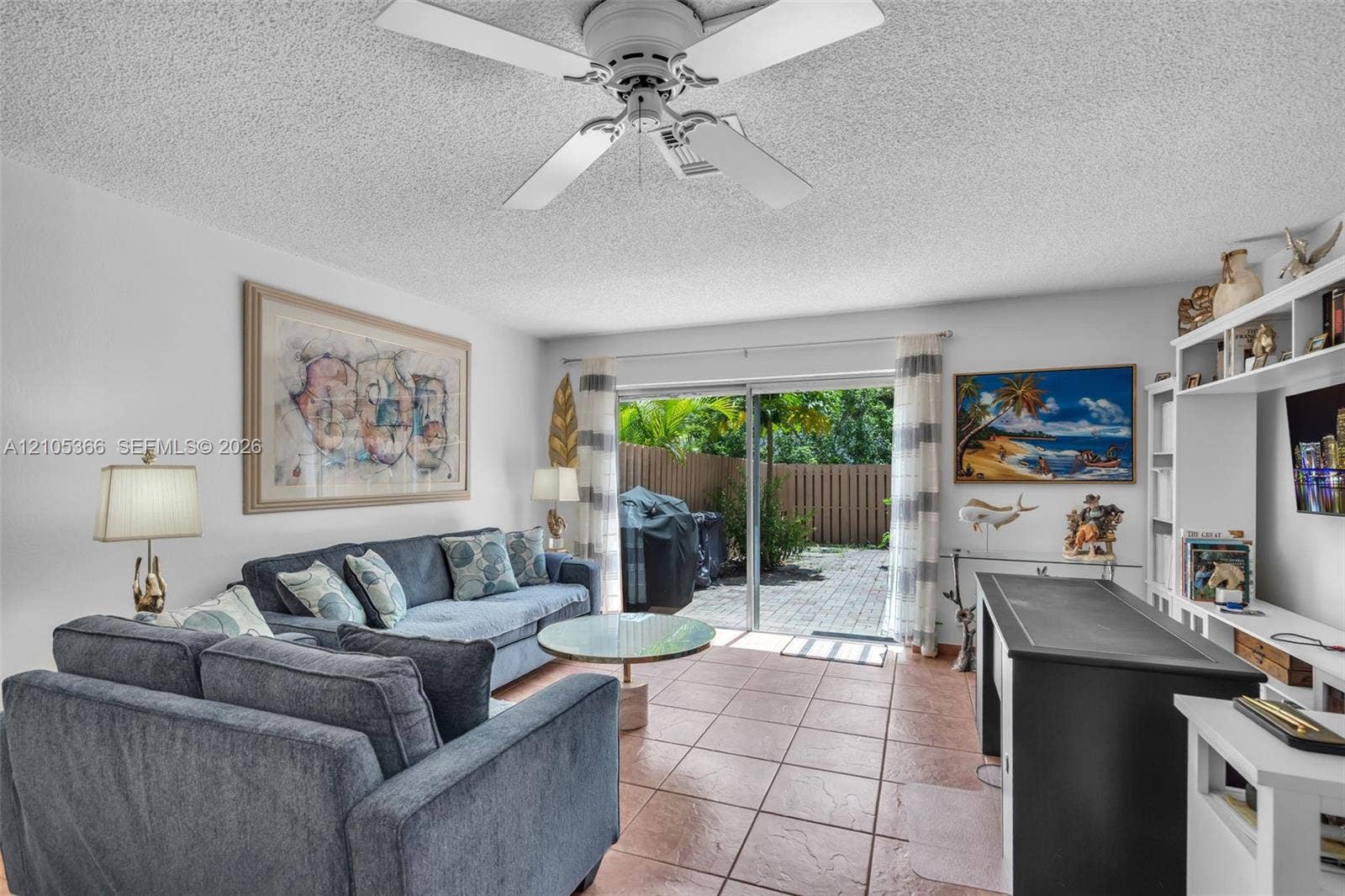 Tiled flooring throughout, sliding glass doors to a private outdoor space, built-in shelving and cabinetry, and a ceiling fan with integrated lighting