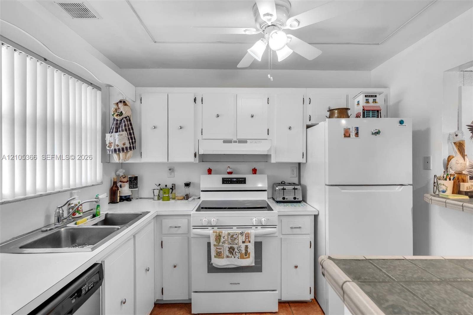U-shaped kitchen with white cabinetry, white appliances, dual basin stainless steel sink, and a ceiling fan with integrated lighting