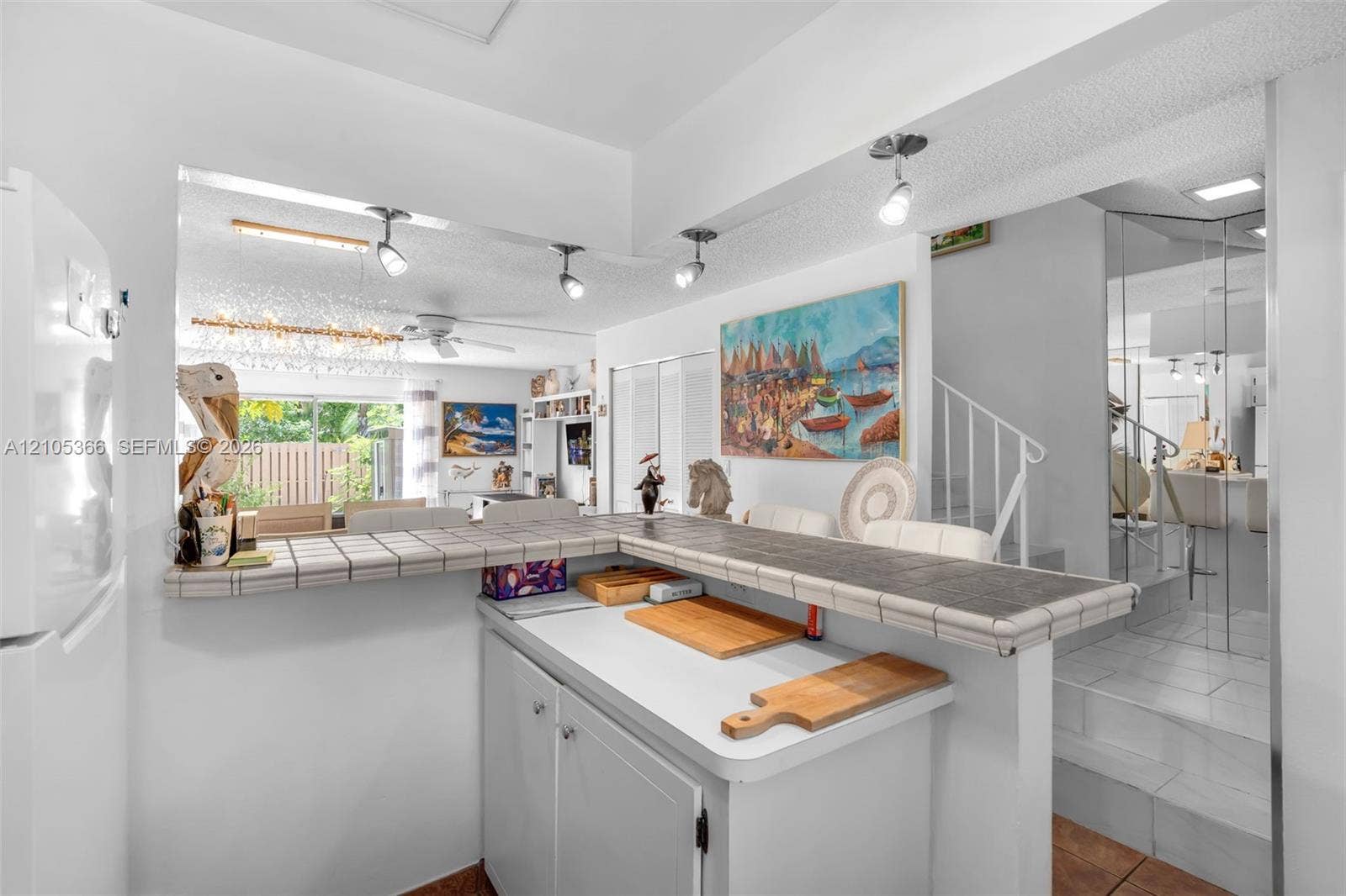 Pass-through window with a tiled countertop, white base cabinetry, and track lighting