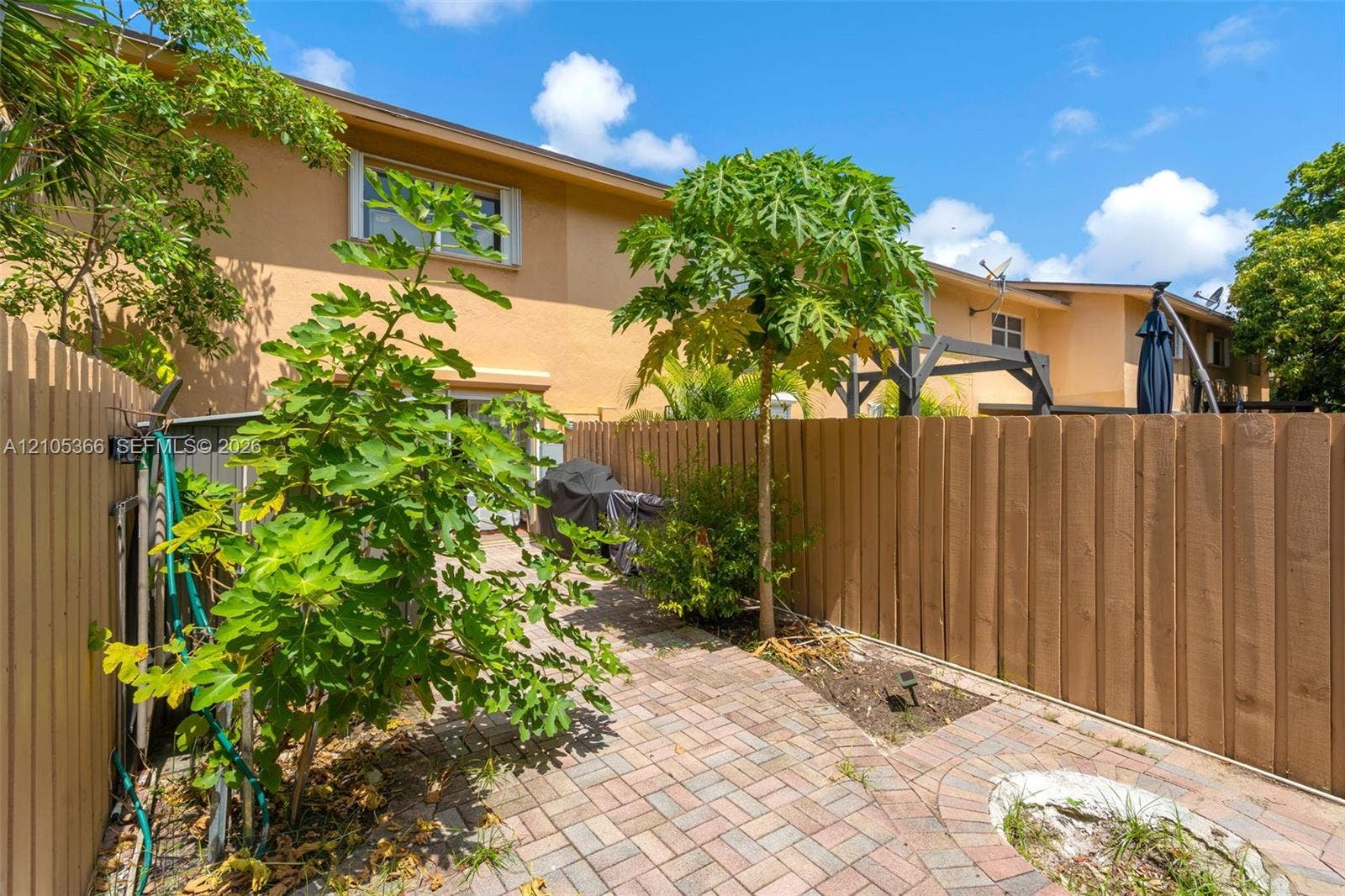 Brick paver patio with a circular design, wood privacy fencing, and established trees