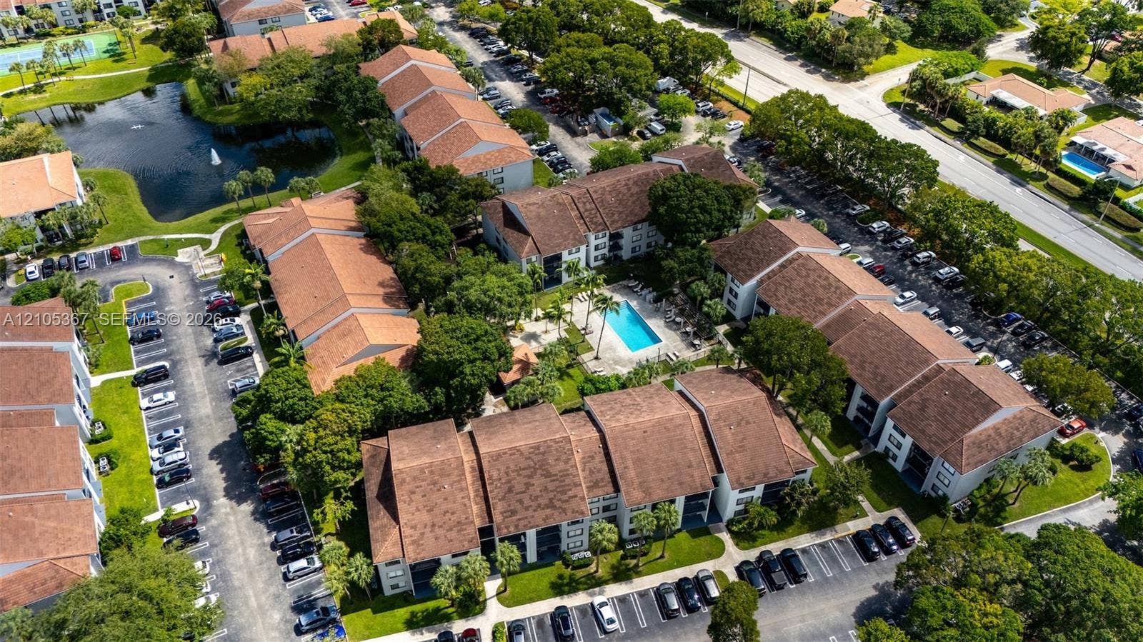 9066 W Atlantic Boulevard, #412, Coral Springs, FL 33071 Aerial view of a residential complex featuring tile roofing, an outdoor swimming pool, mature landscaping, and an on-site pond with a fountain